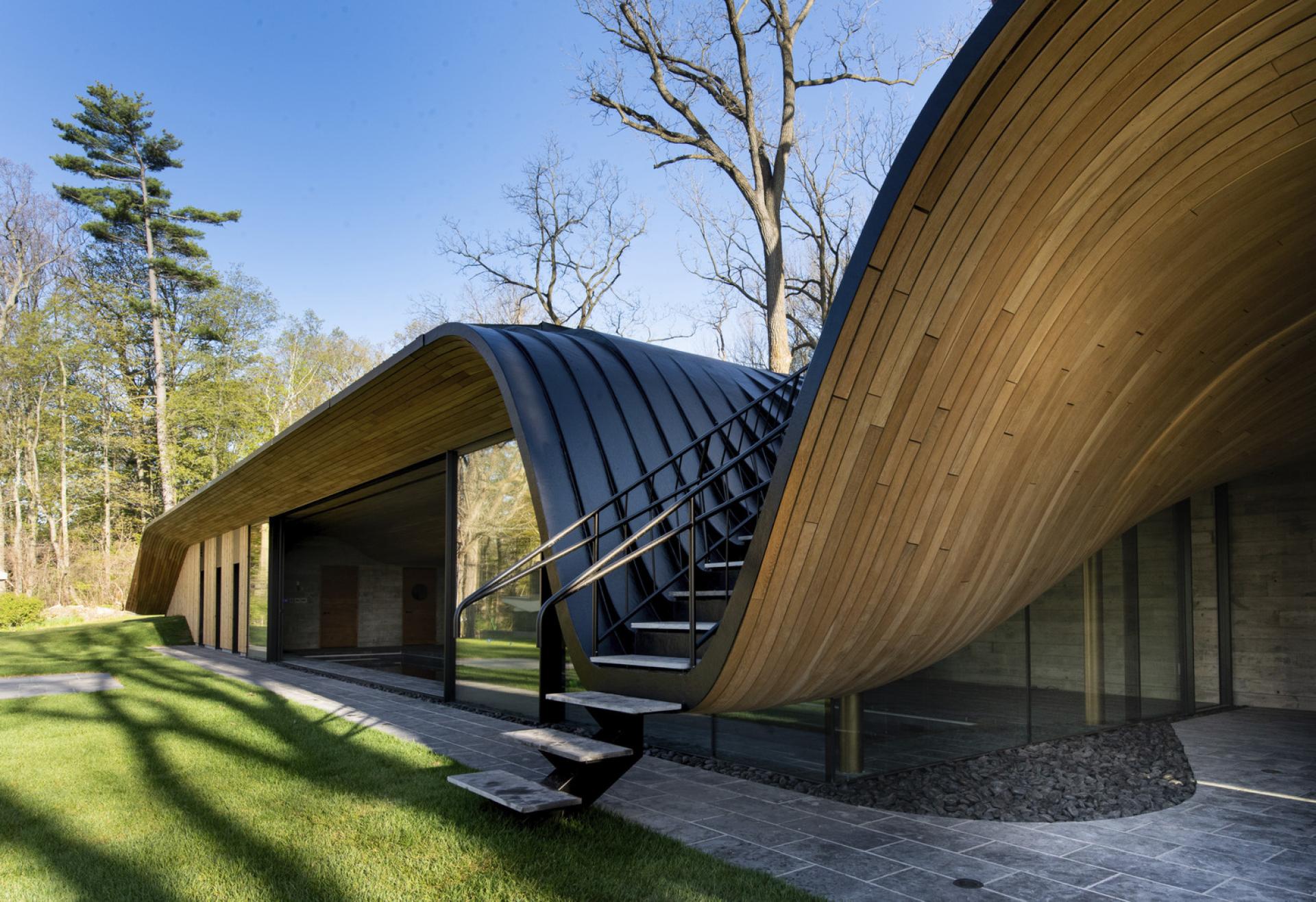 Sleek, modern Fold House in Southern Ontario features unique curved wooden and metal roofing harmonizing with the natural landscape.