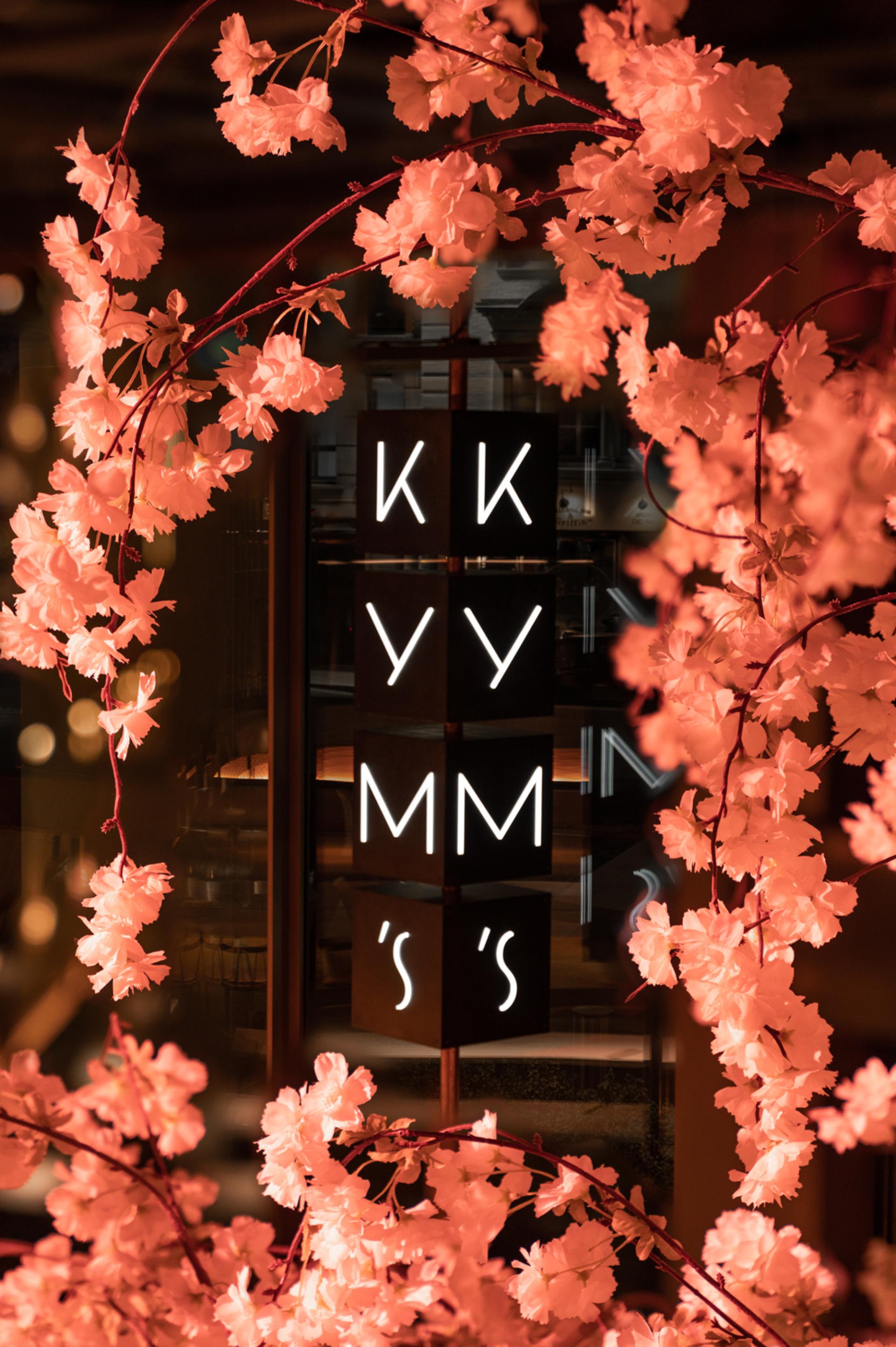 Elegant illuminated sign displaying "KKYYMM's" framed by soft pink cherry blossom branches at Andrew Wong's restaurant.