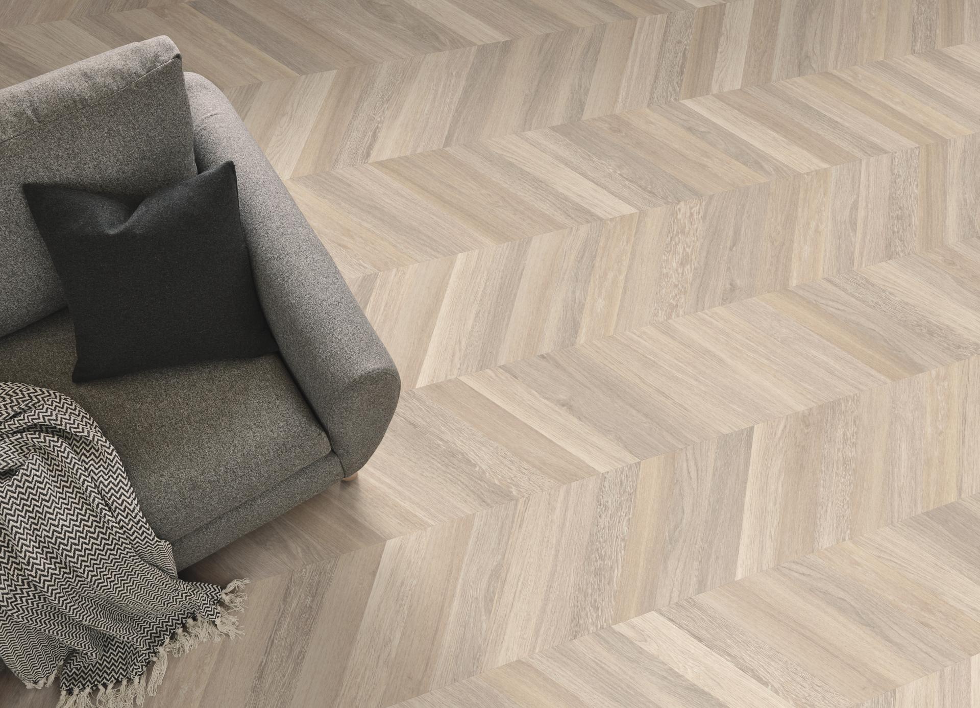 Stylish gray sofa with a black pillow on a modern chevron wood-patterned floor from Karndean's Van Gogh collection.