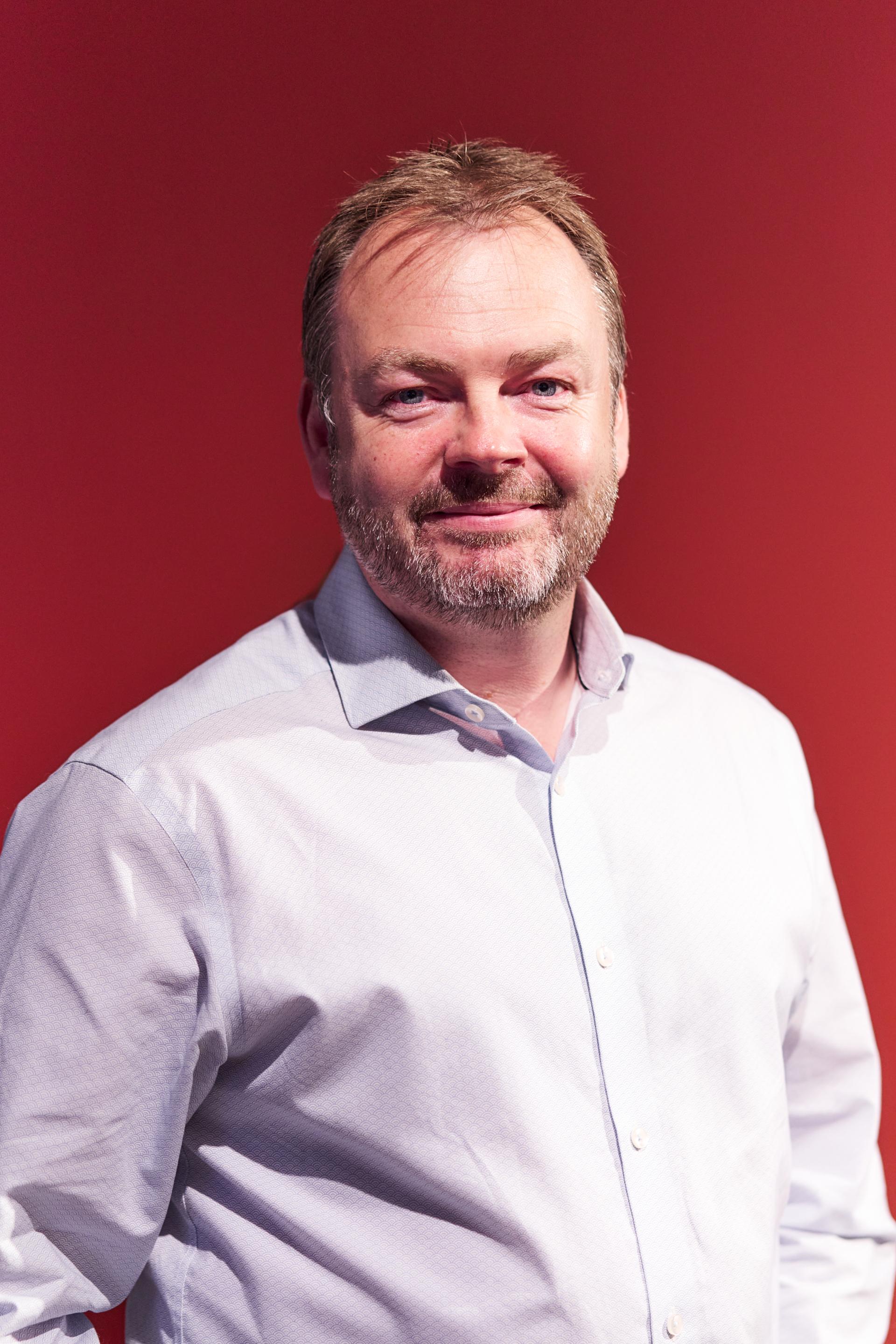 A smiling man in a light blue shirt poses against a red backdrop, reflecting discussions on Glasgow's residential mix.