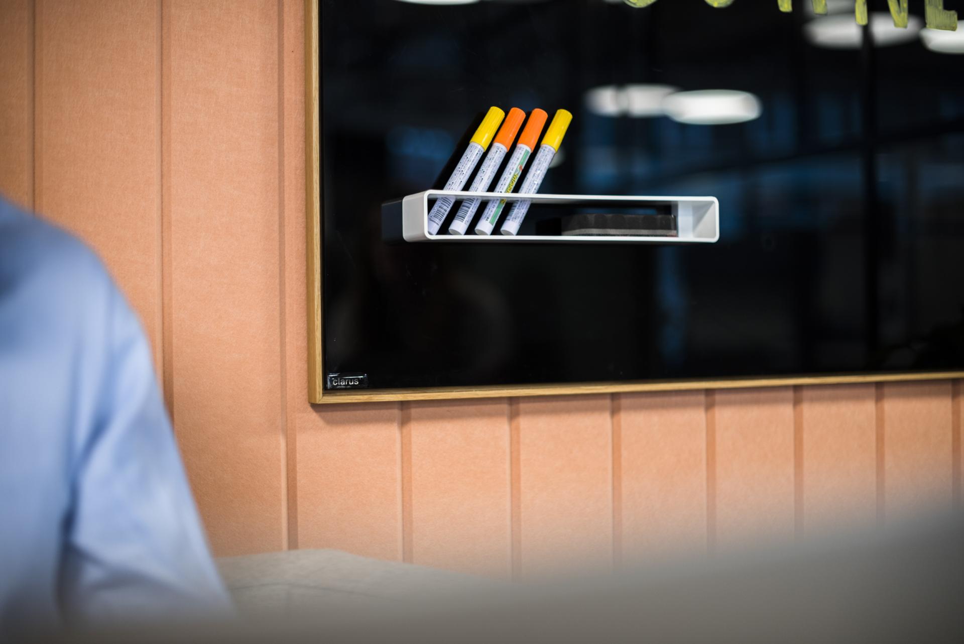 Recycled PET acoustic paneling in a modern showroom, featuring colorful markers on a sleek wall-mounted holder.