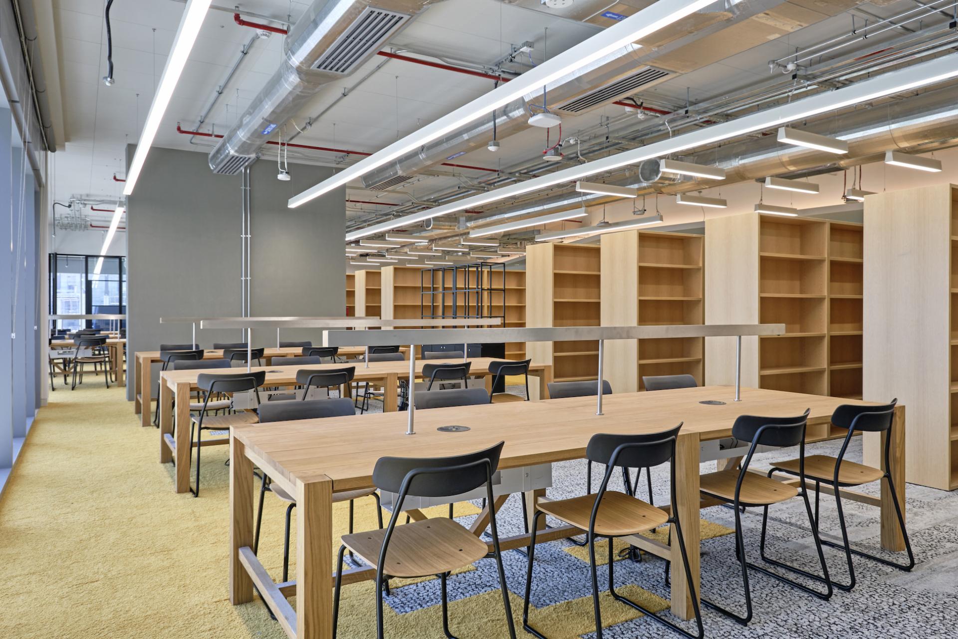 Modern study space in the new Heriot-Watt University campus, featuring wooden tables, black chairs, and shelving.
