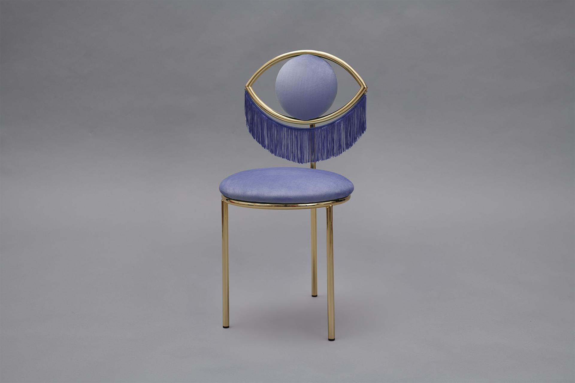 Wink chair designed by Masquespacio features a golden frame and eye-shaped backrest accented with purple fringe.