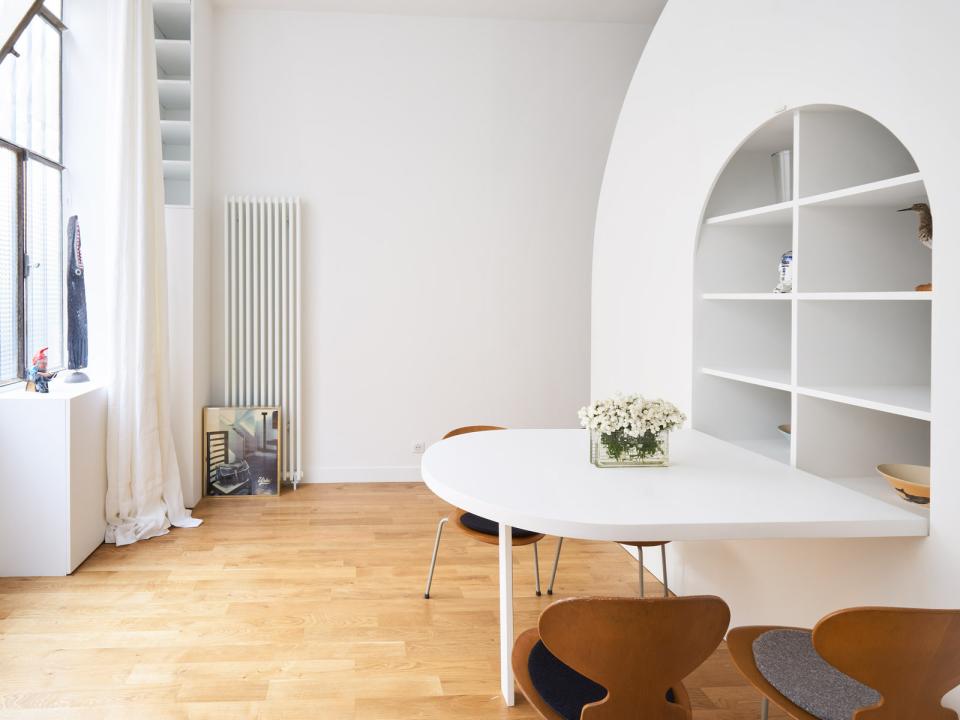 Stylish Parisian interior featuring a white table, wooden chairs, and decorative shelves, showcasing flexible living space design.