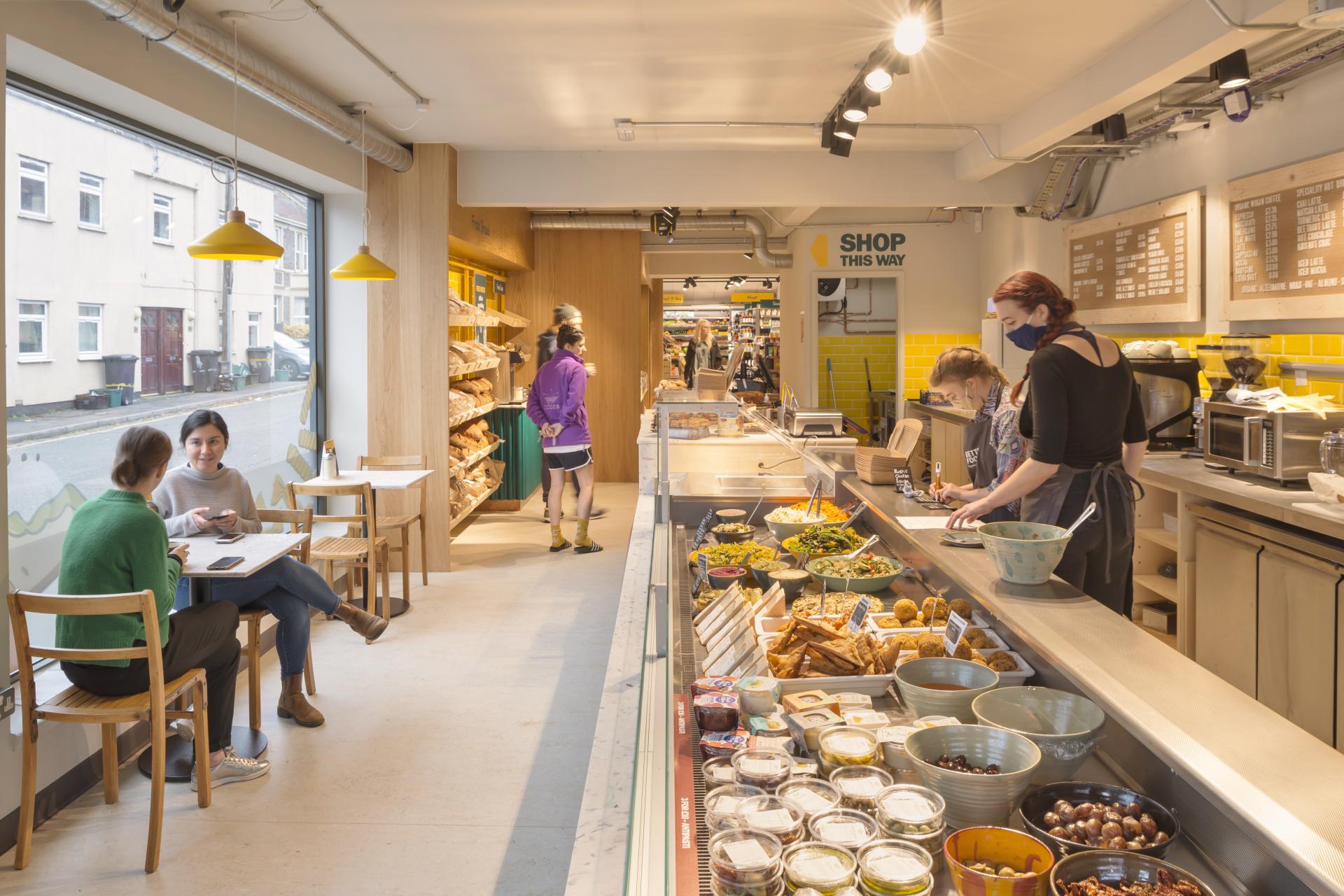 Bright and inviting café-deli interior of Better Food store on Gloucester Road, showcasing fresh produce and customers enjoying the space.