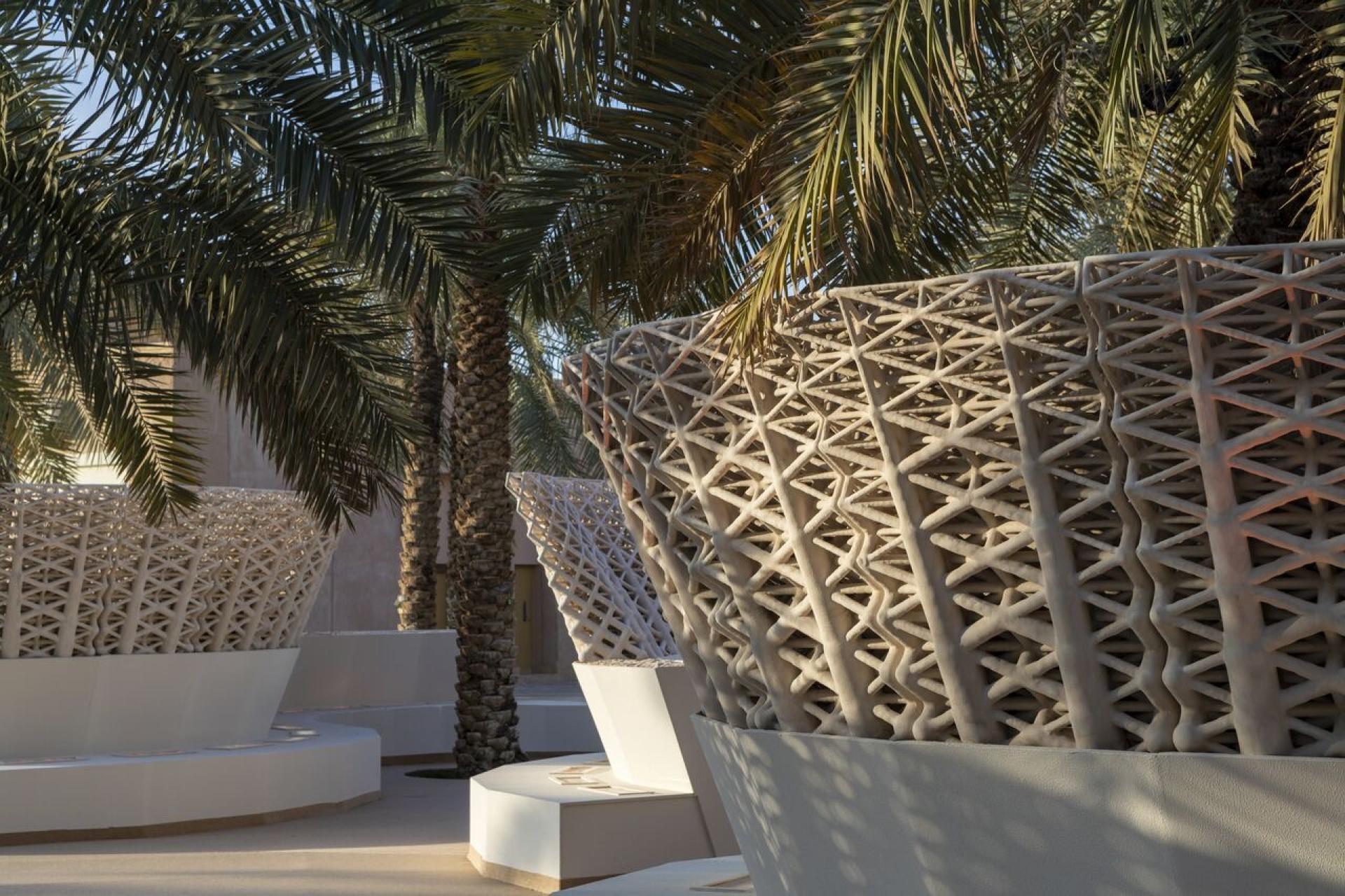3D-printed architectural planters surrounded by palm trees in a modern outdoor space, showcasing innovative construction techniques.