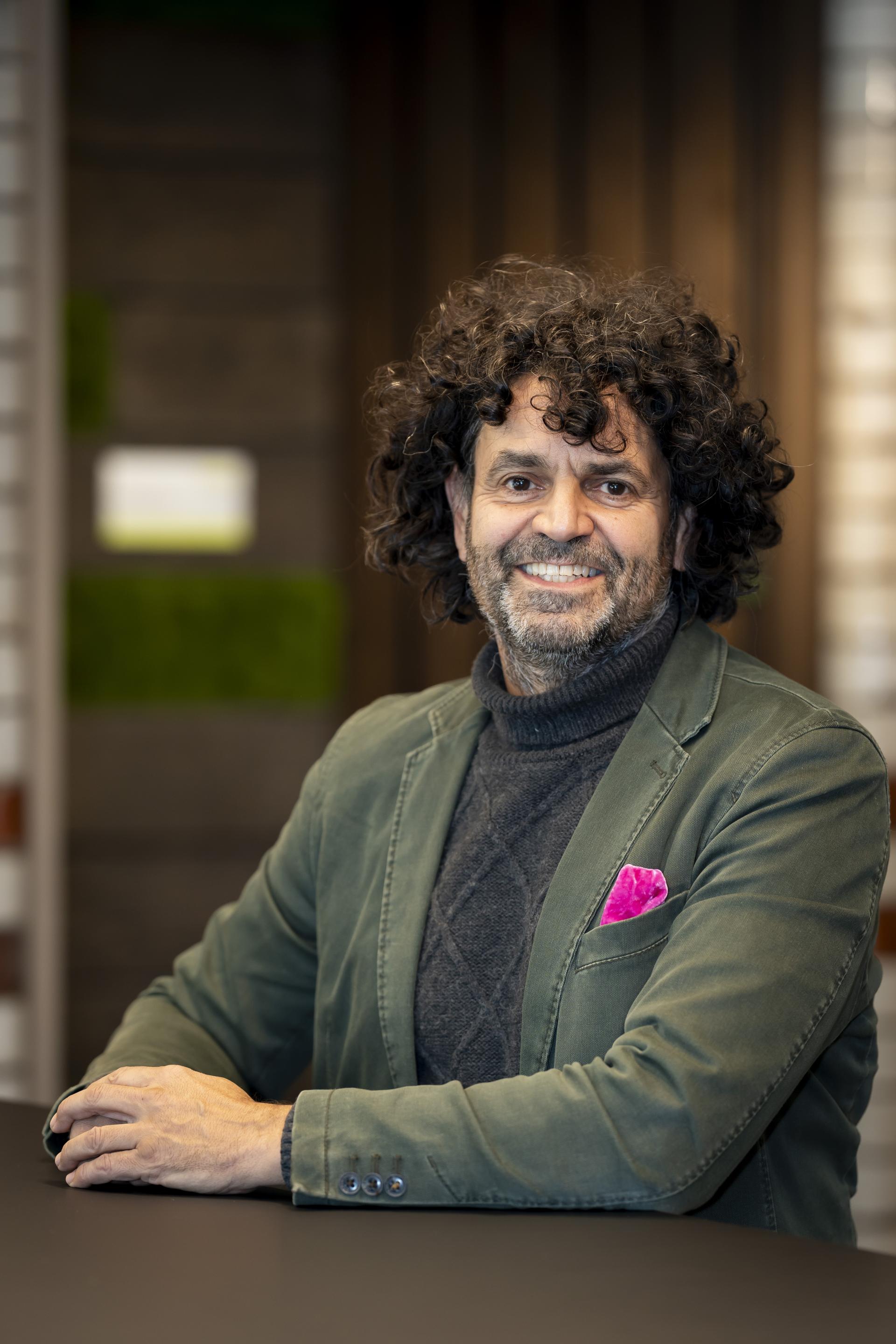 Experienced designer in a green jacket, smiling at a table, reflecting technology's role in sustainable design solutions.