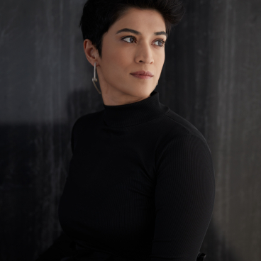 Pallavi Dean, founder of Roar studio, poses in a sleek black outfit against a textured backdrop, exuding confidence.