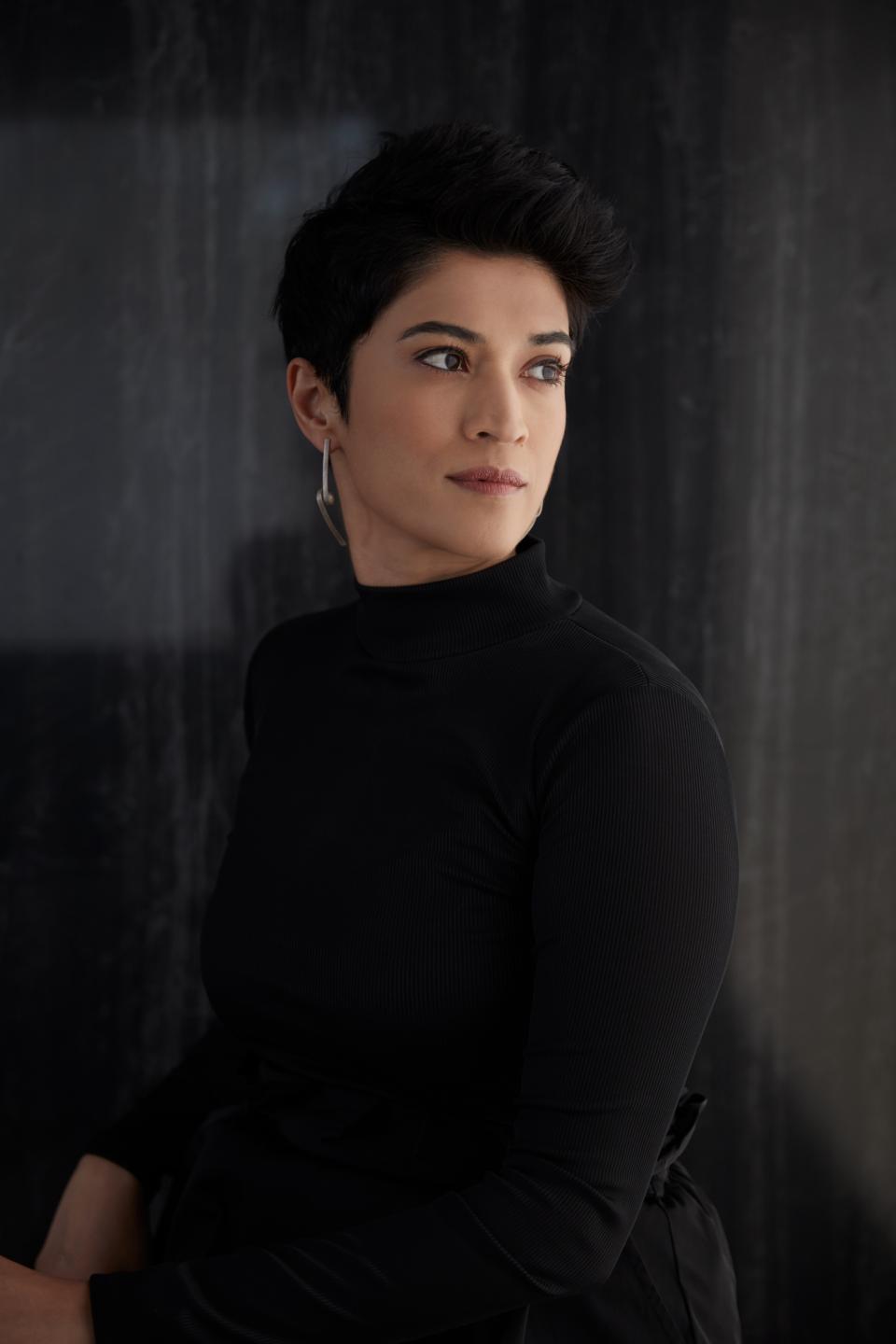 Pallavi Dean, founder of Roar studio, poses in a sleek black outfit against a textured backdrop, exuding confidence.
