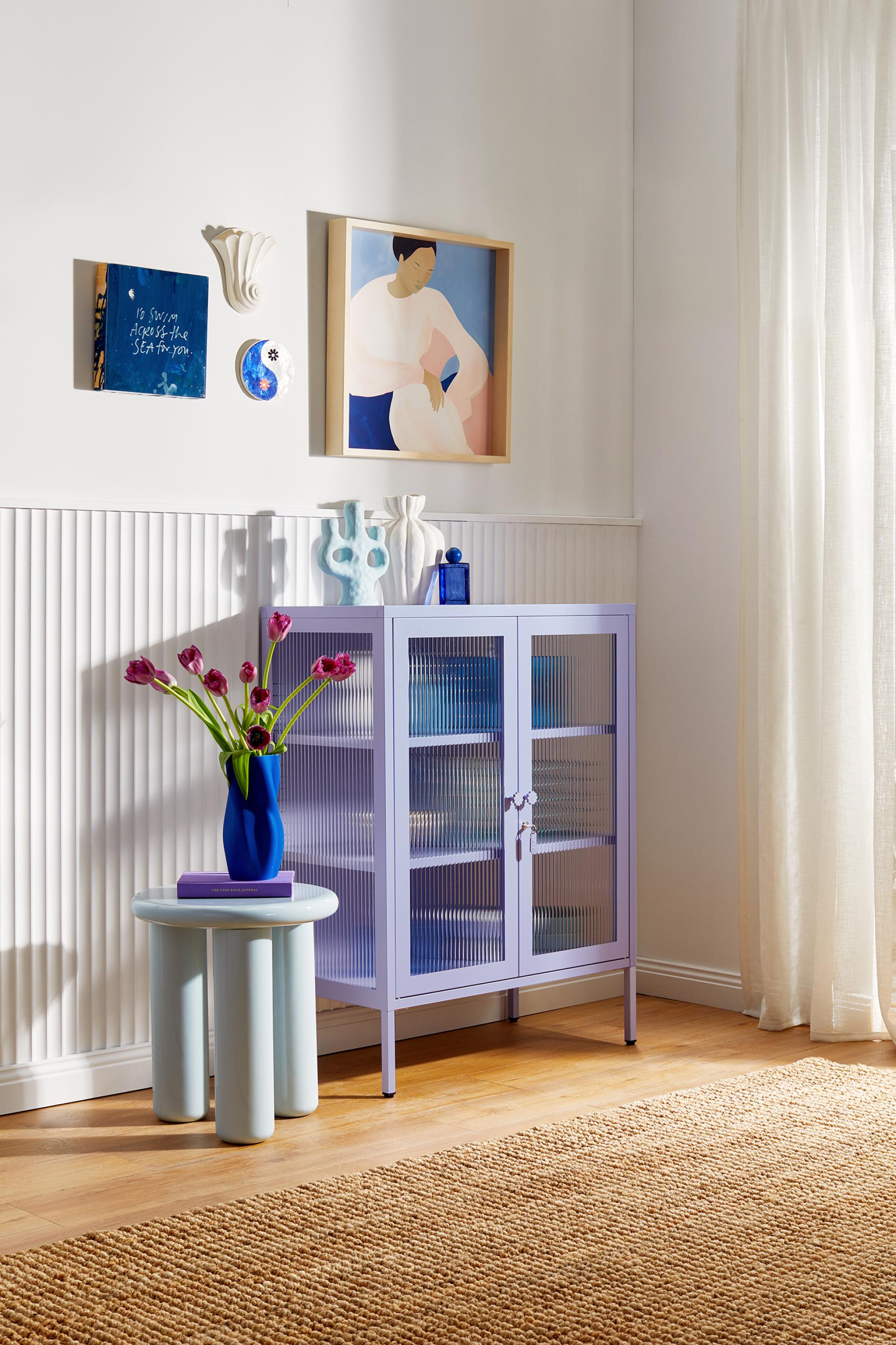 Playful pastel purple cabinet from Mustard Made's Glass Collection, adorned with vibrant flowers and modern decor in a stylish interior.