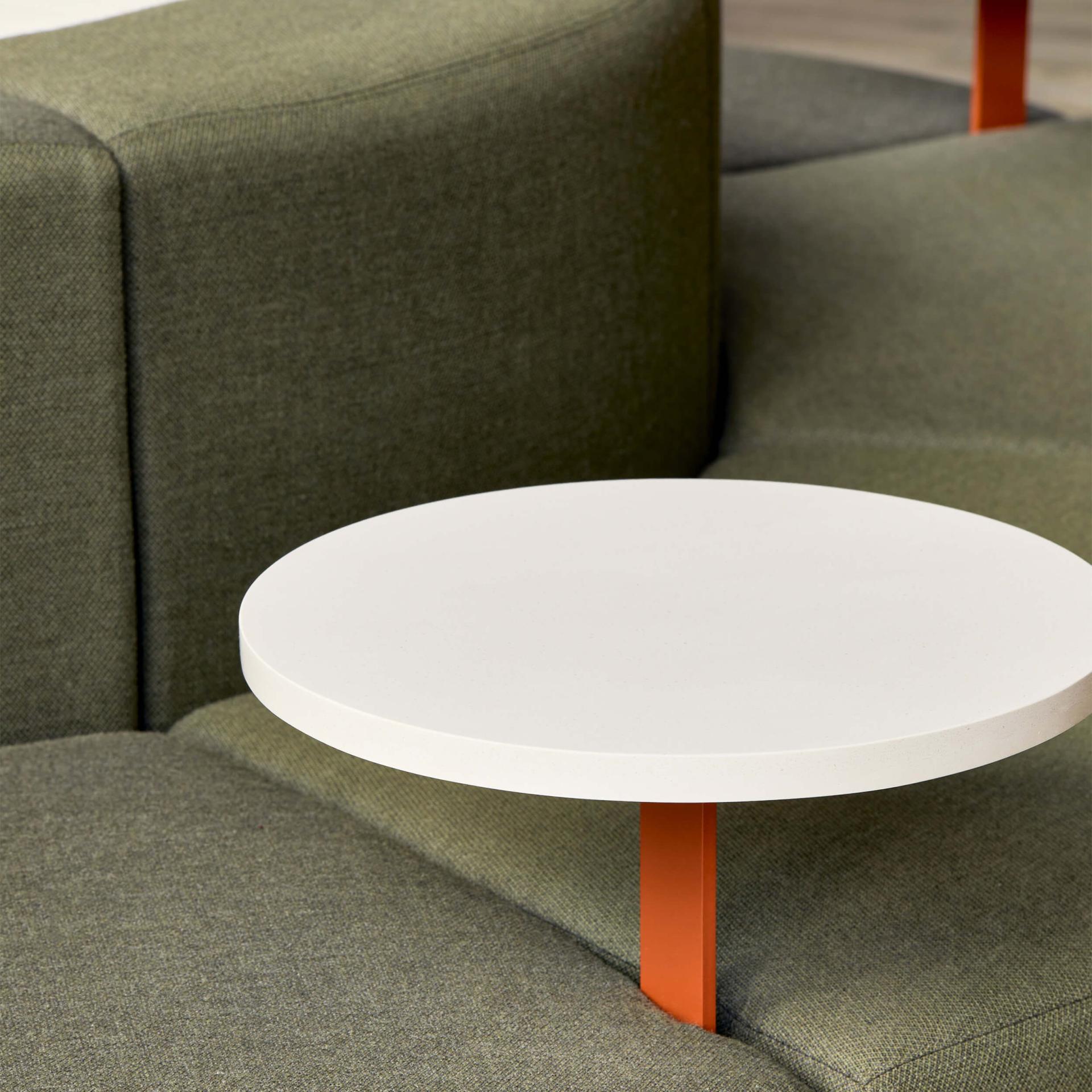Contemporary seating with a round white table on an olive green upholstered sofa, showcasing innovative design and materiality.
