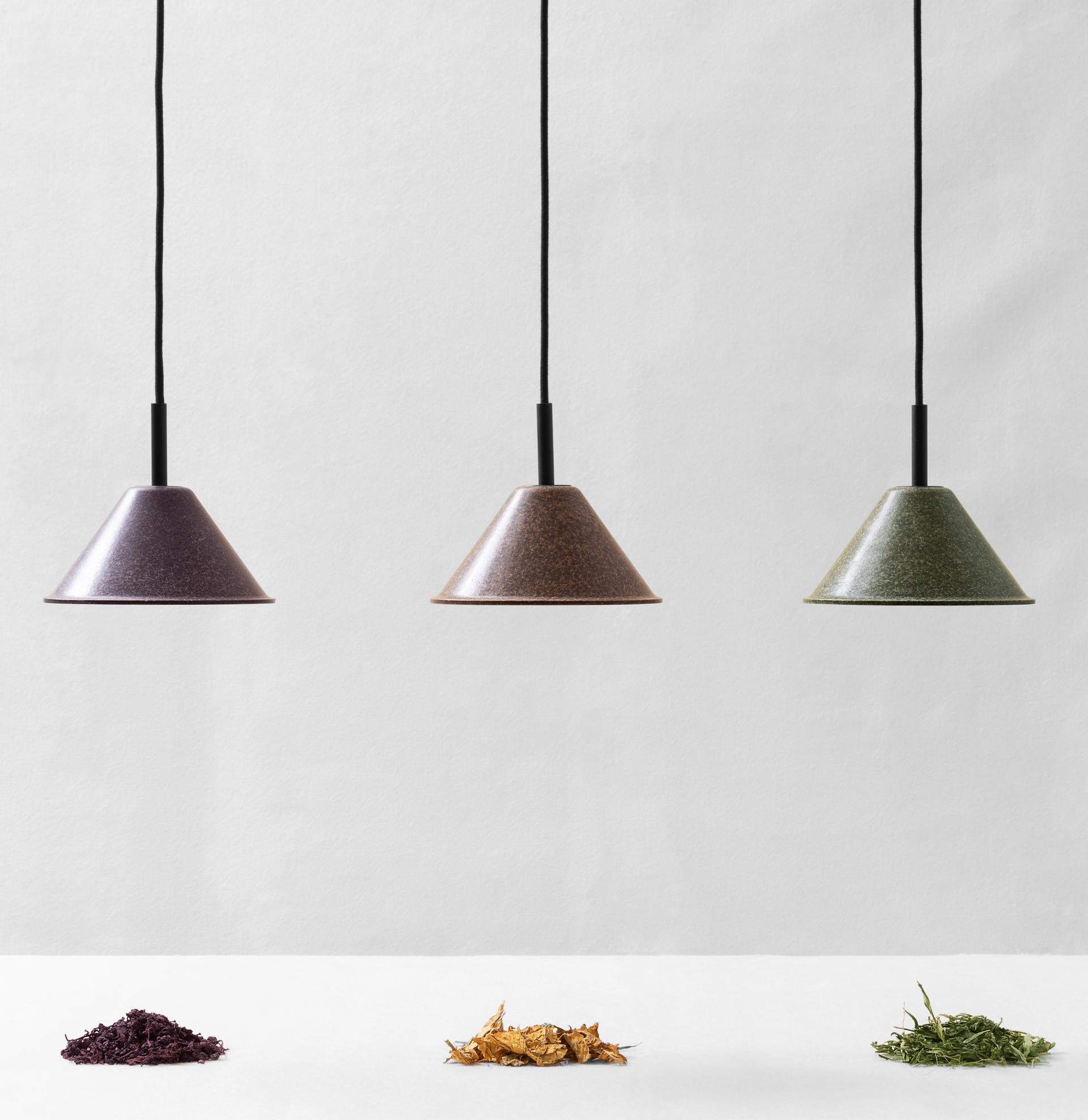 Sustainable design: three modern pendant lights hang above piles of colorful, natural materials representing eco-friendly craftsmanship.