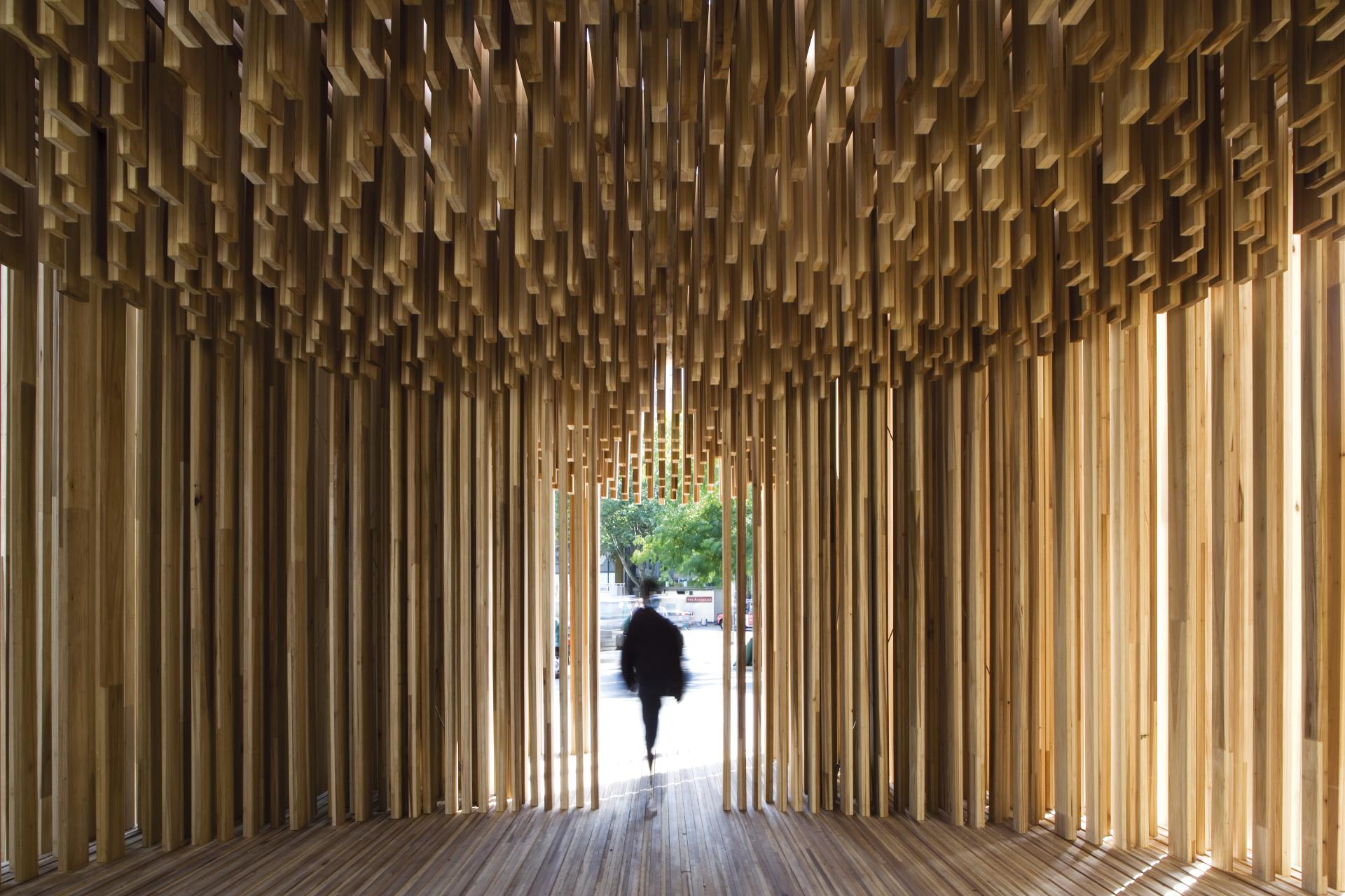 A person walks through an installation with wooden slats, reflecting contemporary monument design in David Adjaye's exhibition.