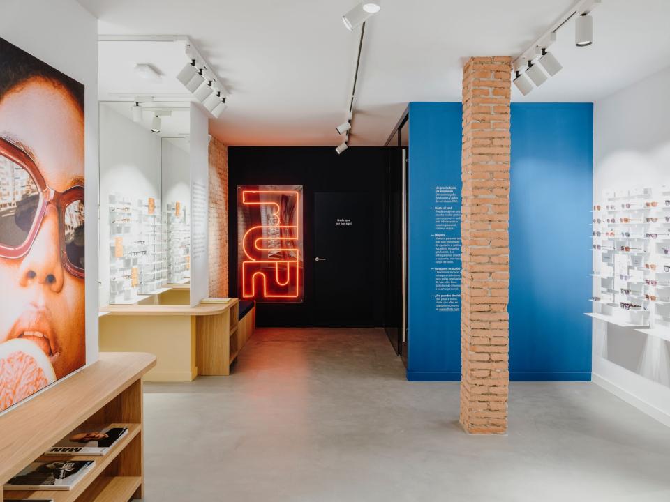 Interior of ACE & TATE Barcelona showcasing sustainable eyewear displays and a vibrant neon sign, emphasizing modern design.