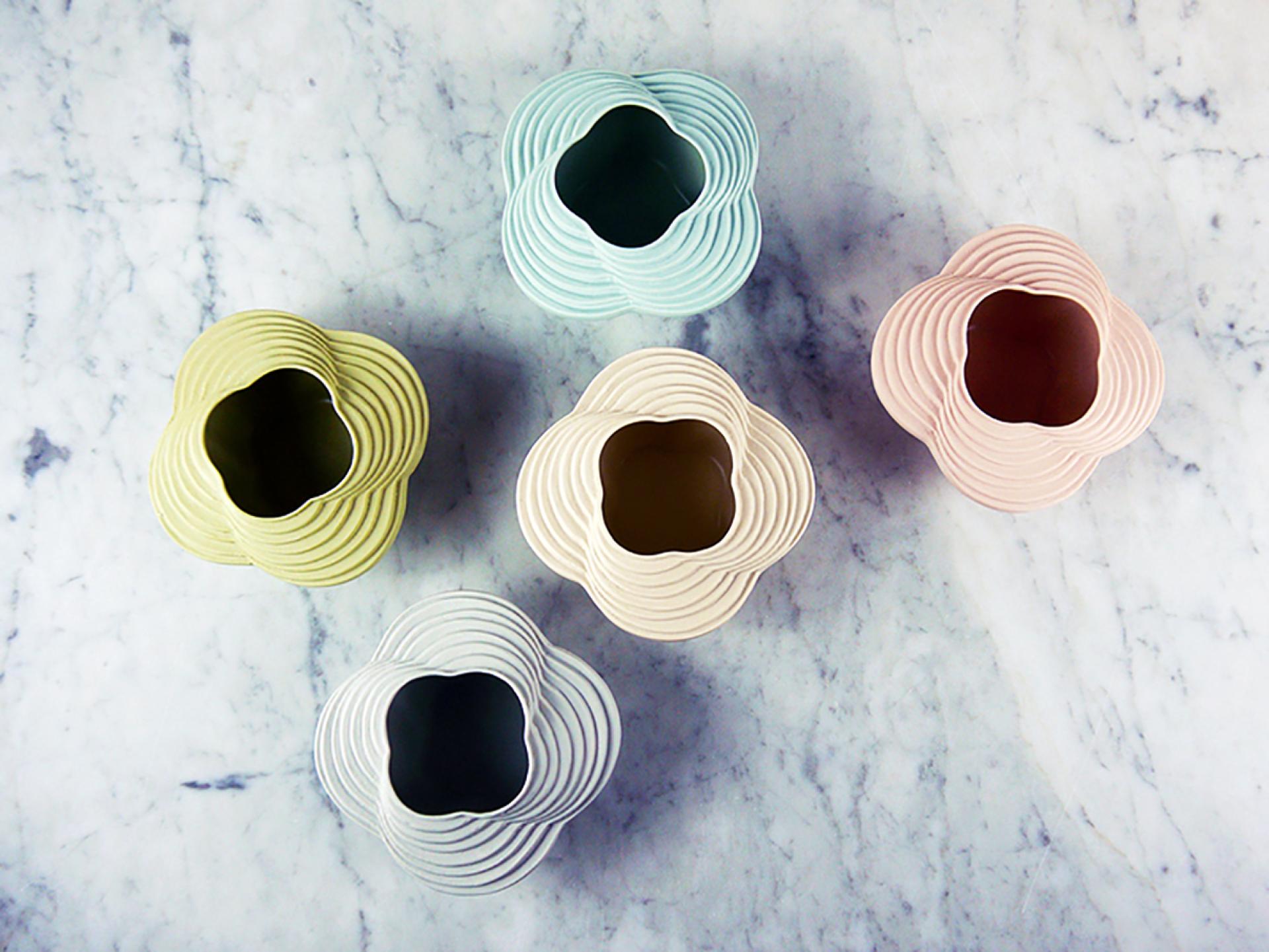 Colorful, layered vases in unique floral shapes displayed on a marble surface, showcasing modern designer craftsmanship.