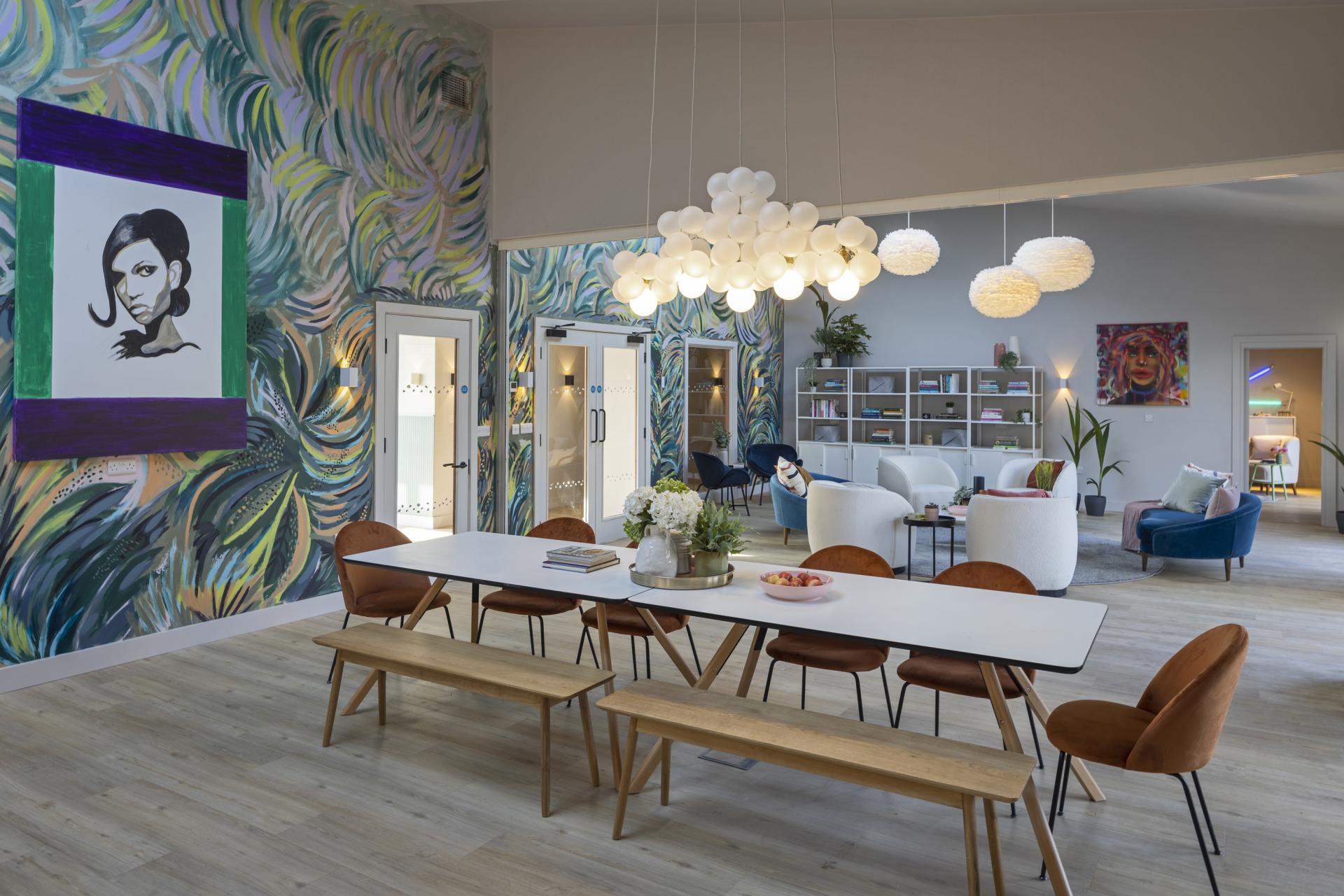 Vibrant interior featuring a dining area with a long table, colorful murals, and stylish seating by Love Interiors.
