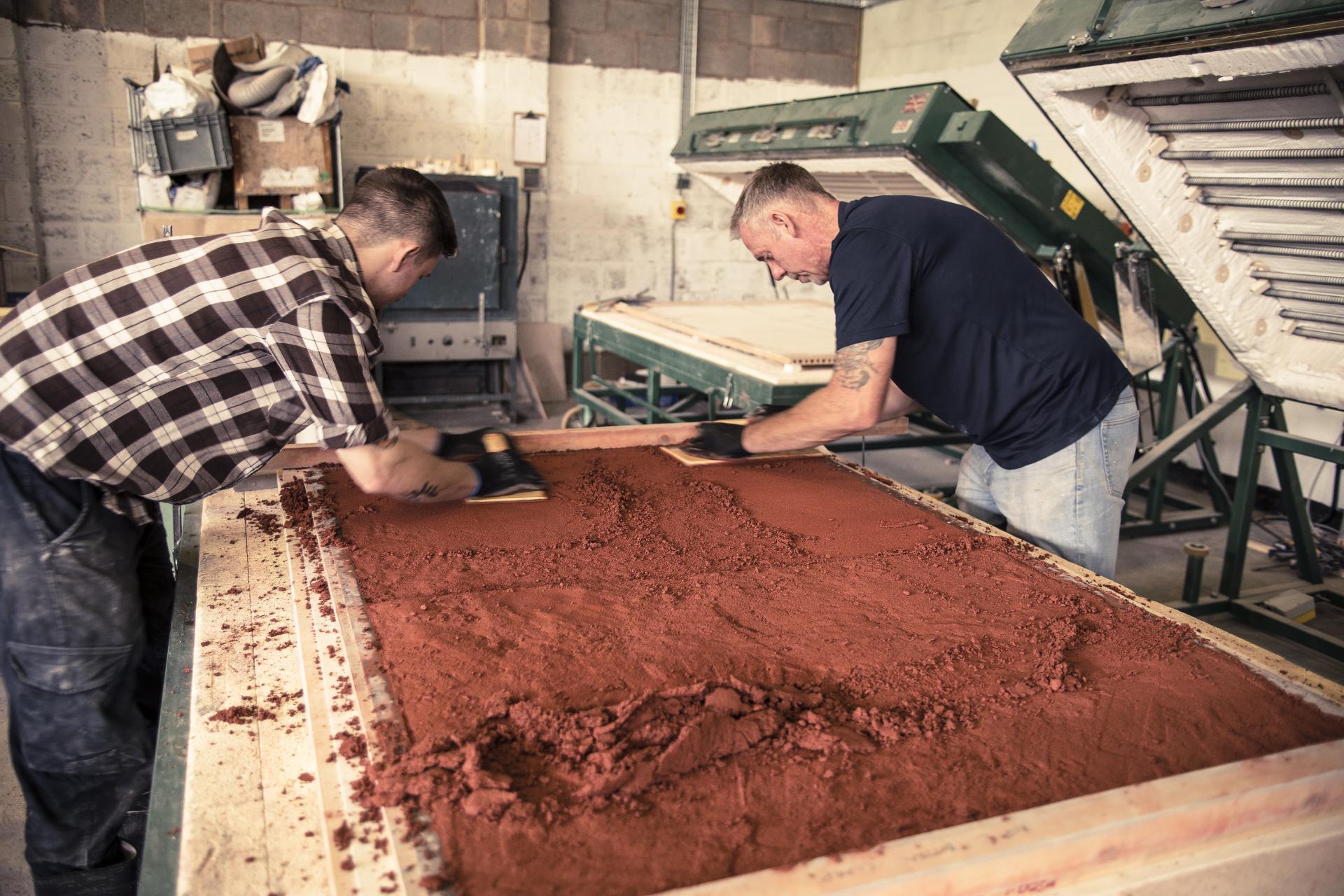 Workers preparing sustainable materials on a flat surface in a workshop, focusing on the application process for Alusid.