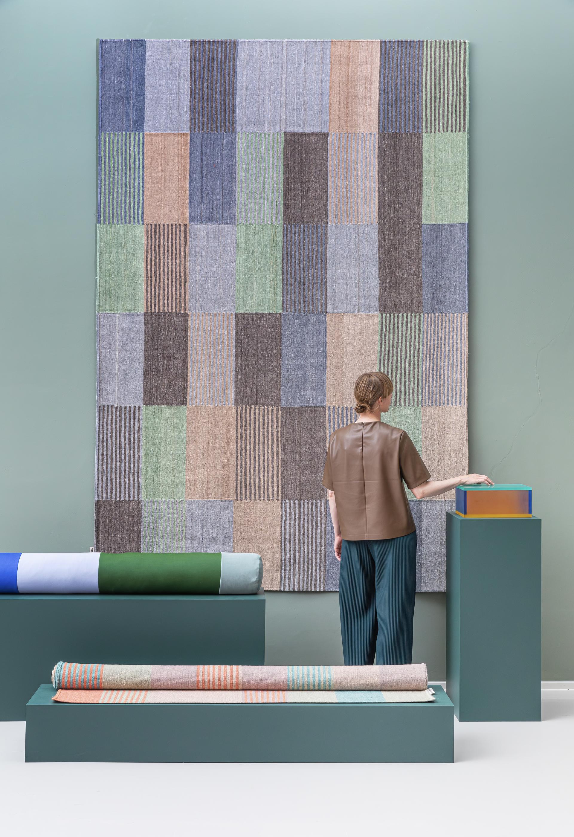 A woman admires vibrant, bio-based textiles displayed in a modern interior, showcasing Raw Color's innovative design.