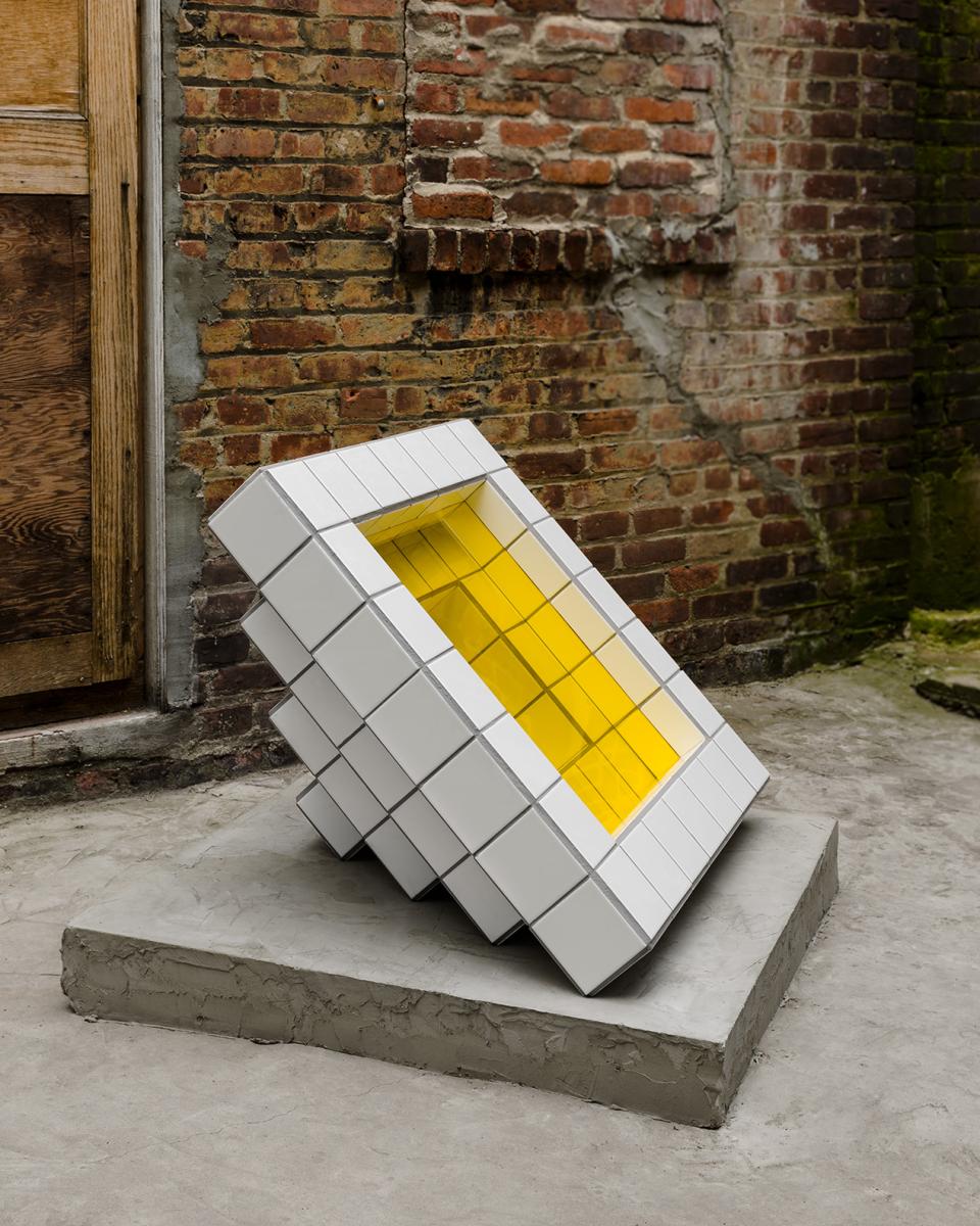 Sculpture by Zac Hacmon featuring white subway tiles and a striking yellow interior, set against a brick wall.