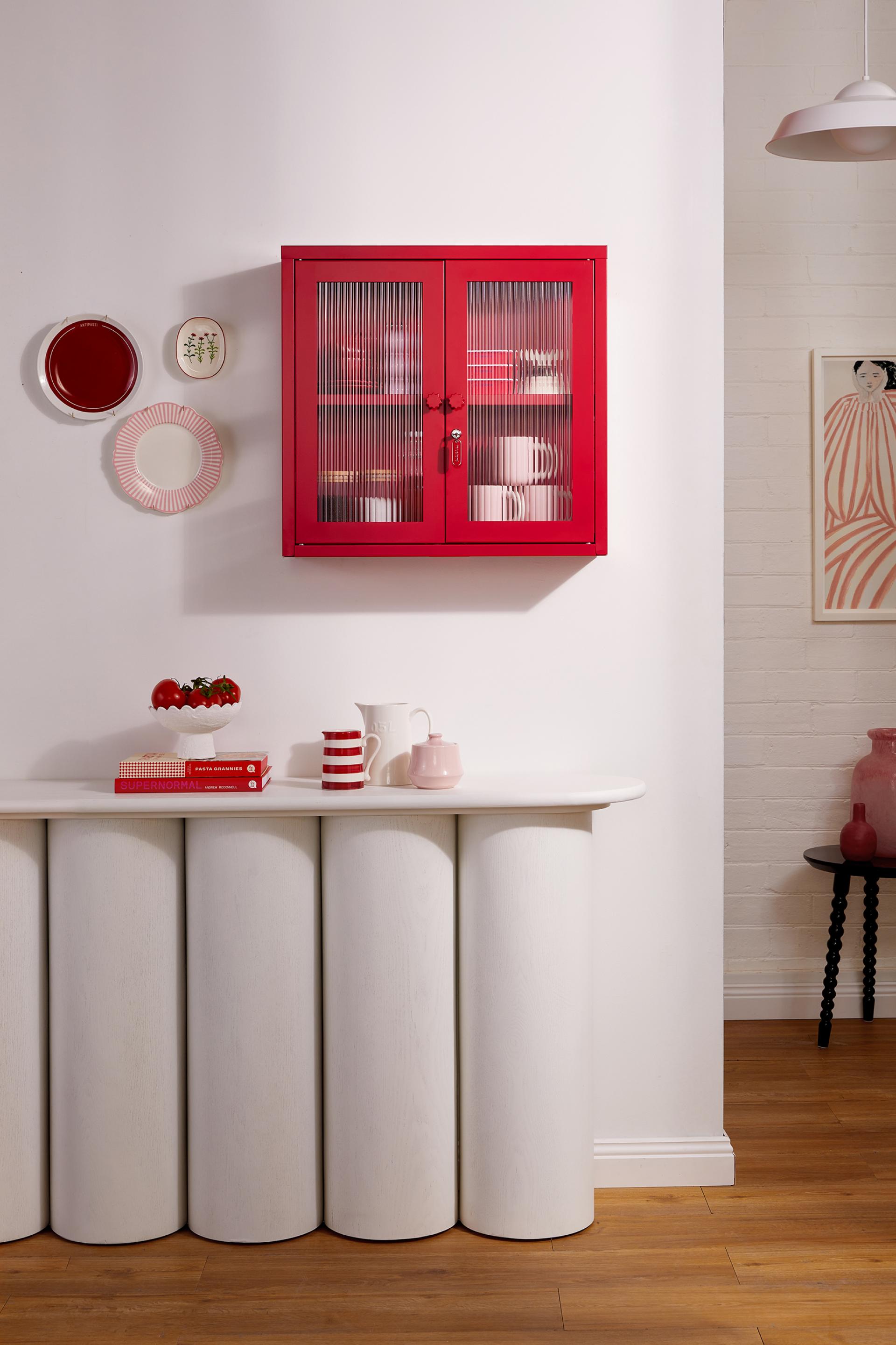 Vibrant red cabinet from Mustard Made's Glass Collection, showcasing playful design with colorful plates and decor on a modern table.