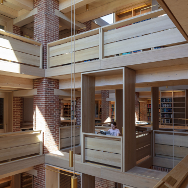 Modern library interior featuring wooden structures, bright natural light, and a girl reading in a cozy nook.