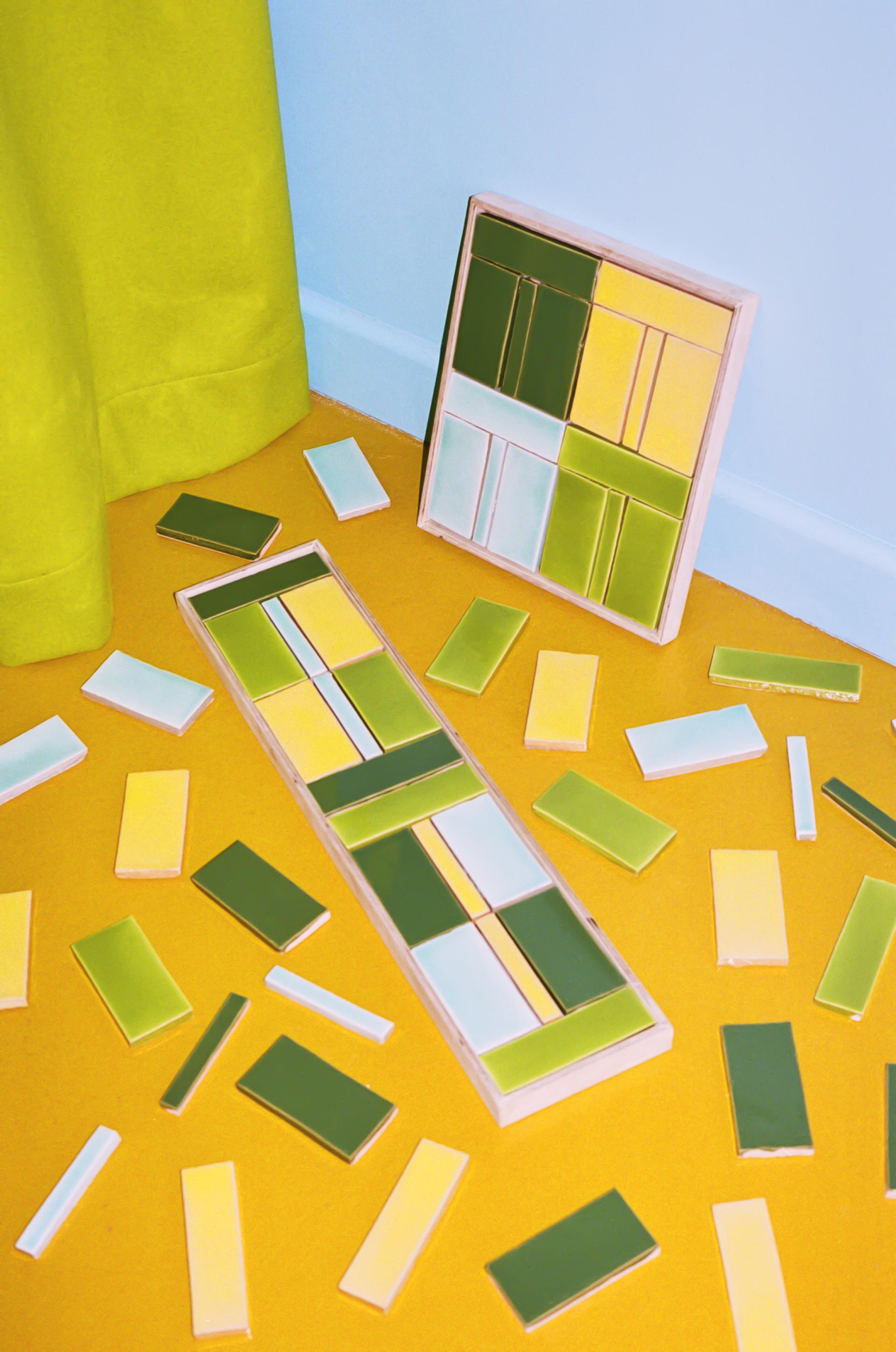 Colorful ceramic tiles in green, yellow, and blue hues scattered on a yellow floor, showcasing Domus and Yinka Ilori's collection.