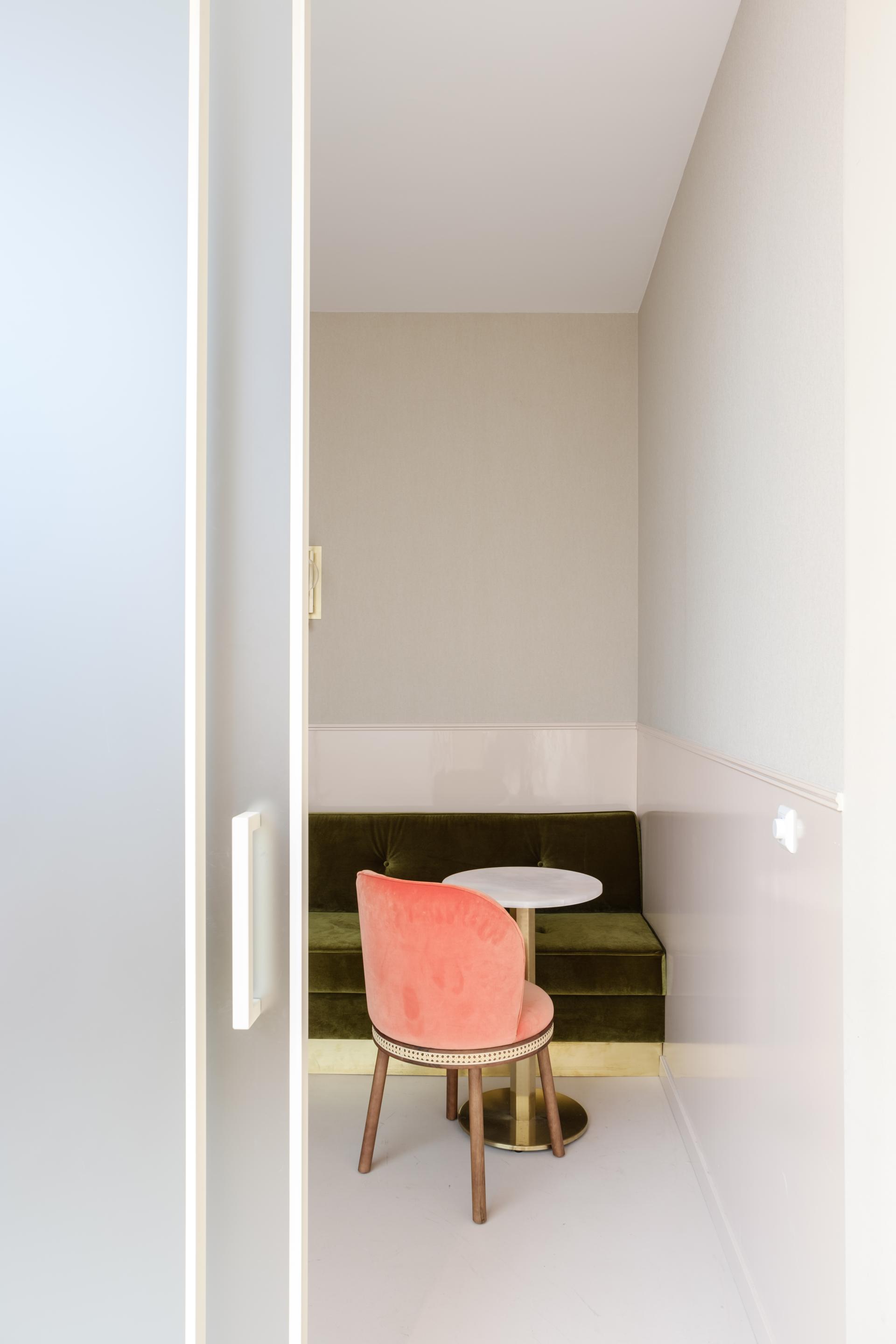 Cozy modern seating area featuring a round white table, pink velvet chair, and green couch in a stylish office design.