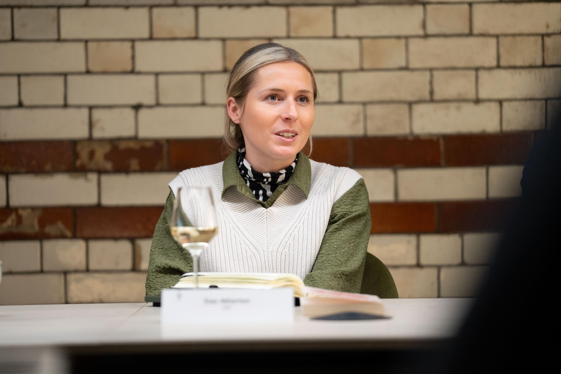 Engaged participant at a roundtable discussion on EDI concepts, wearing a stylish sweater and seated with a notebook.