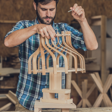 Craftsman assembling a bespoke wooden lampshade inspired by art deco design in a workshop.