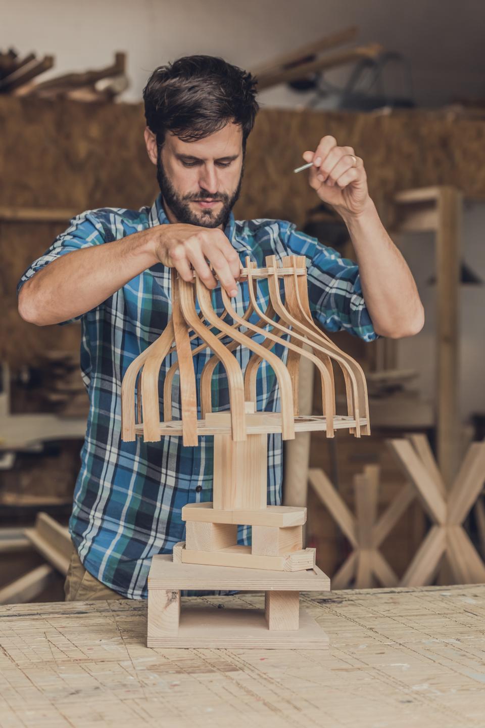 Craftsman assembling a bespoke wooden lampshade inspired by art deco design in a workshop.