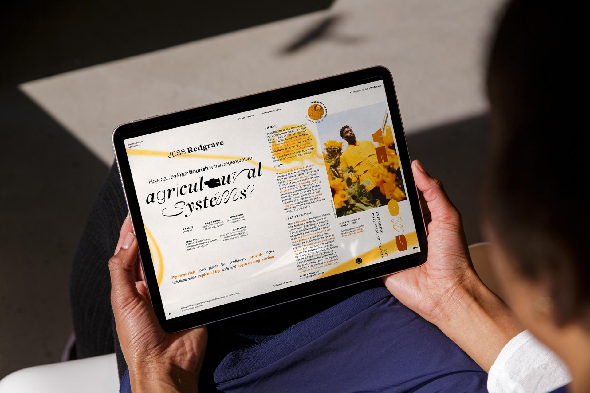 A person holds a tablet displaying an article on color's role in regenerative agricultural systems.