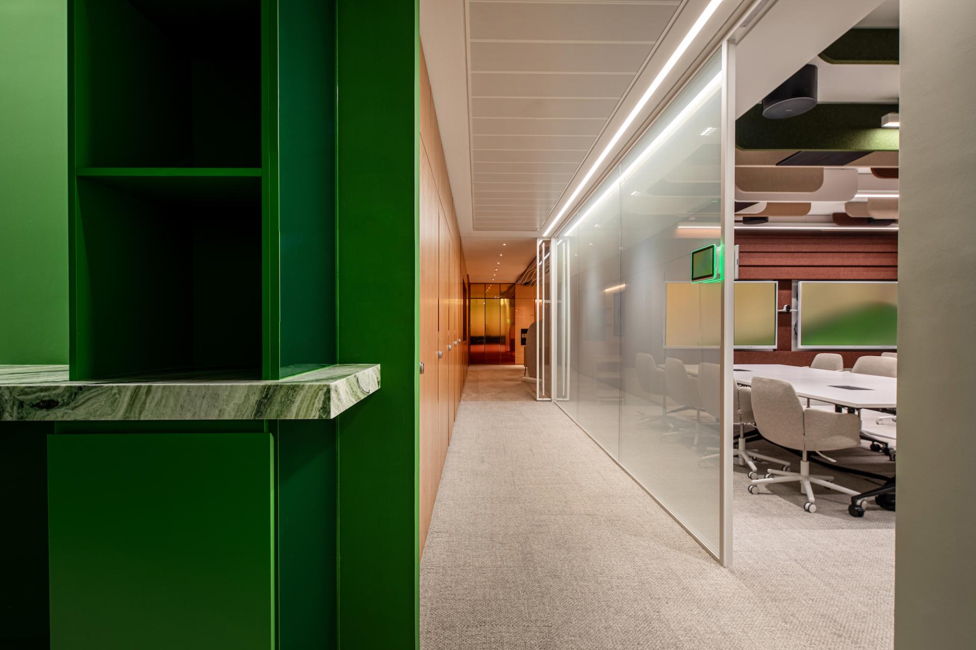 Vibrant green office corridor leading to a modern meeting room, showcasing a blend of nature-inspired design elements.