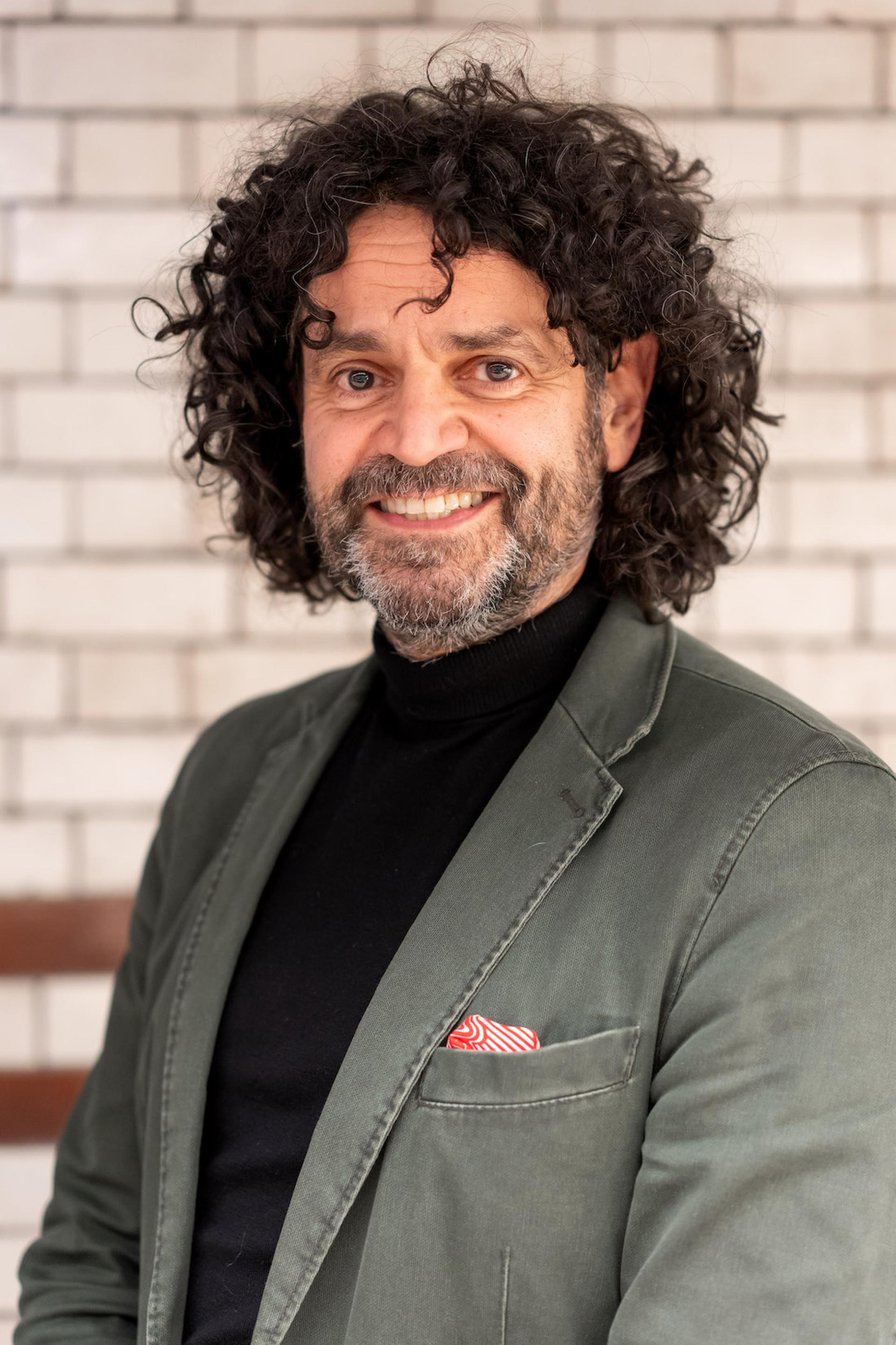 Confident man in a green blazer and black turtleneck, discussing sustainability and value engineering at a roundtable event.