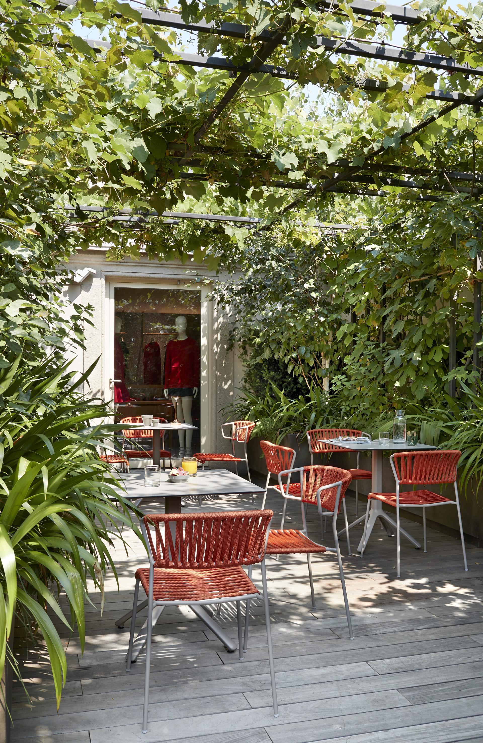 Stylish outdoor café setting featuring SCAB Design's Lisa chairs surrounded by lush greenery and vibrant decor.