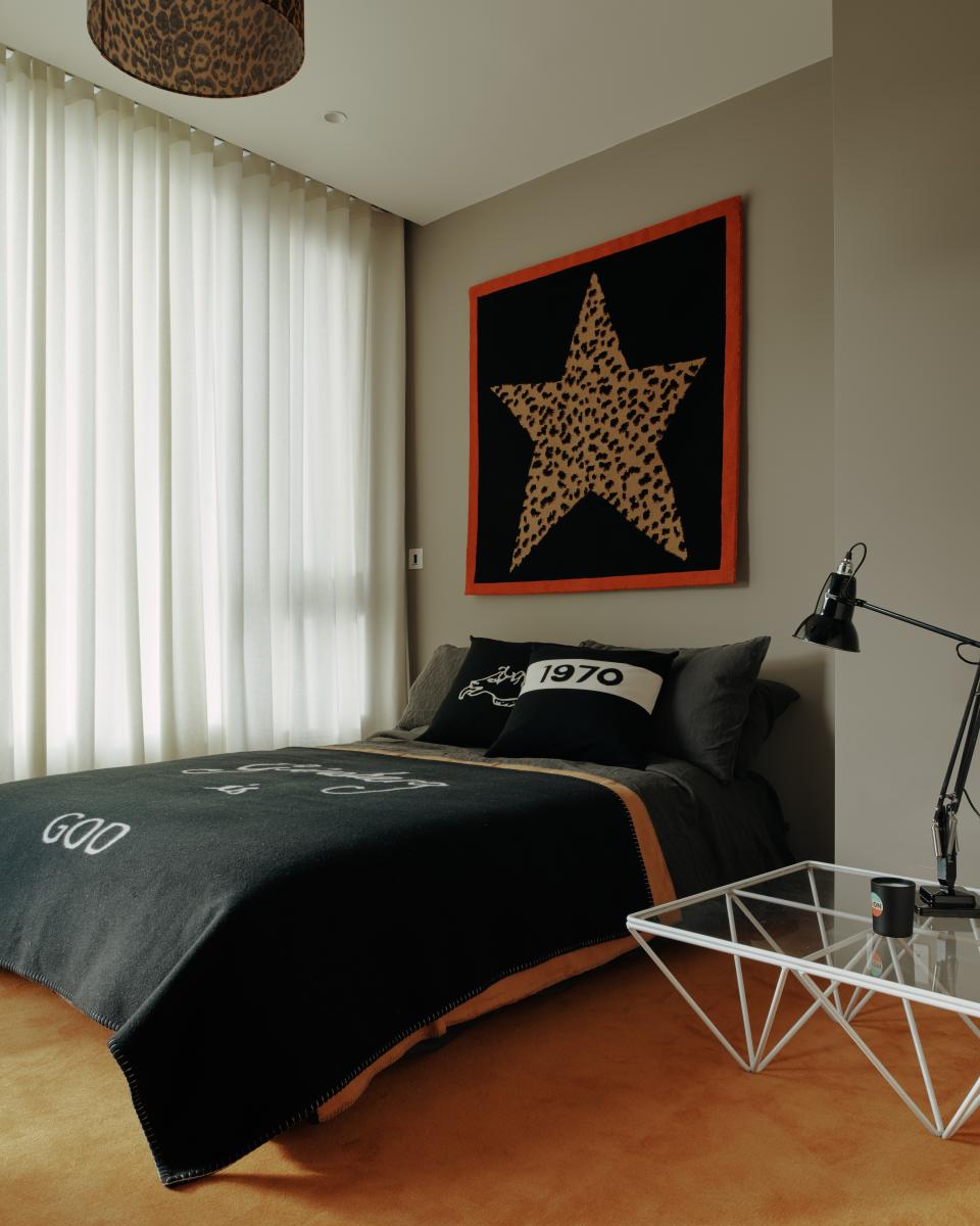Stylish bedroom featuring a leopard-print star tapestry, black bedspread, and modern geometric furniture in warm tones.
