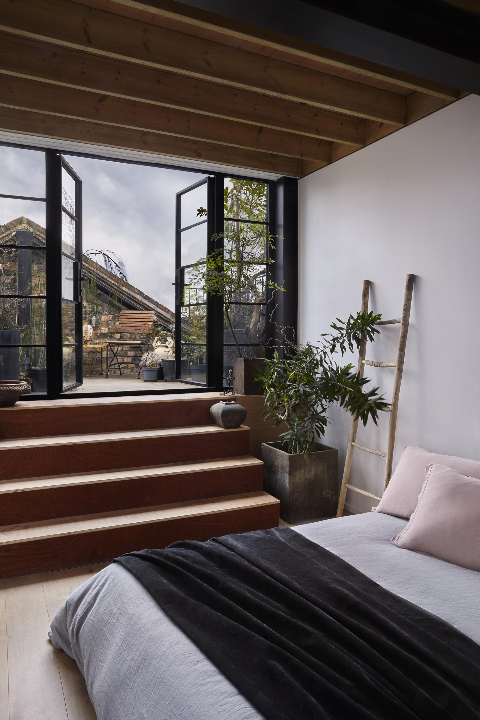 Modern bedroom interior showcasing natural light, wooden steps, and greenery, reflecting THISS's focus on sustainable design principles.