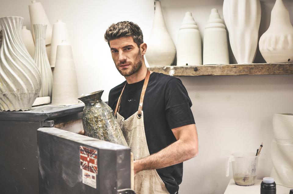 Ceramicist Ryan Barrett holding a handcrafted vase in his studio, surrounded by artistic pottery and tools.