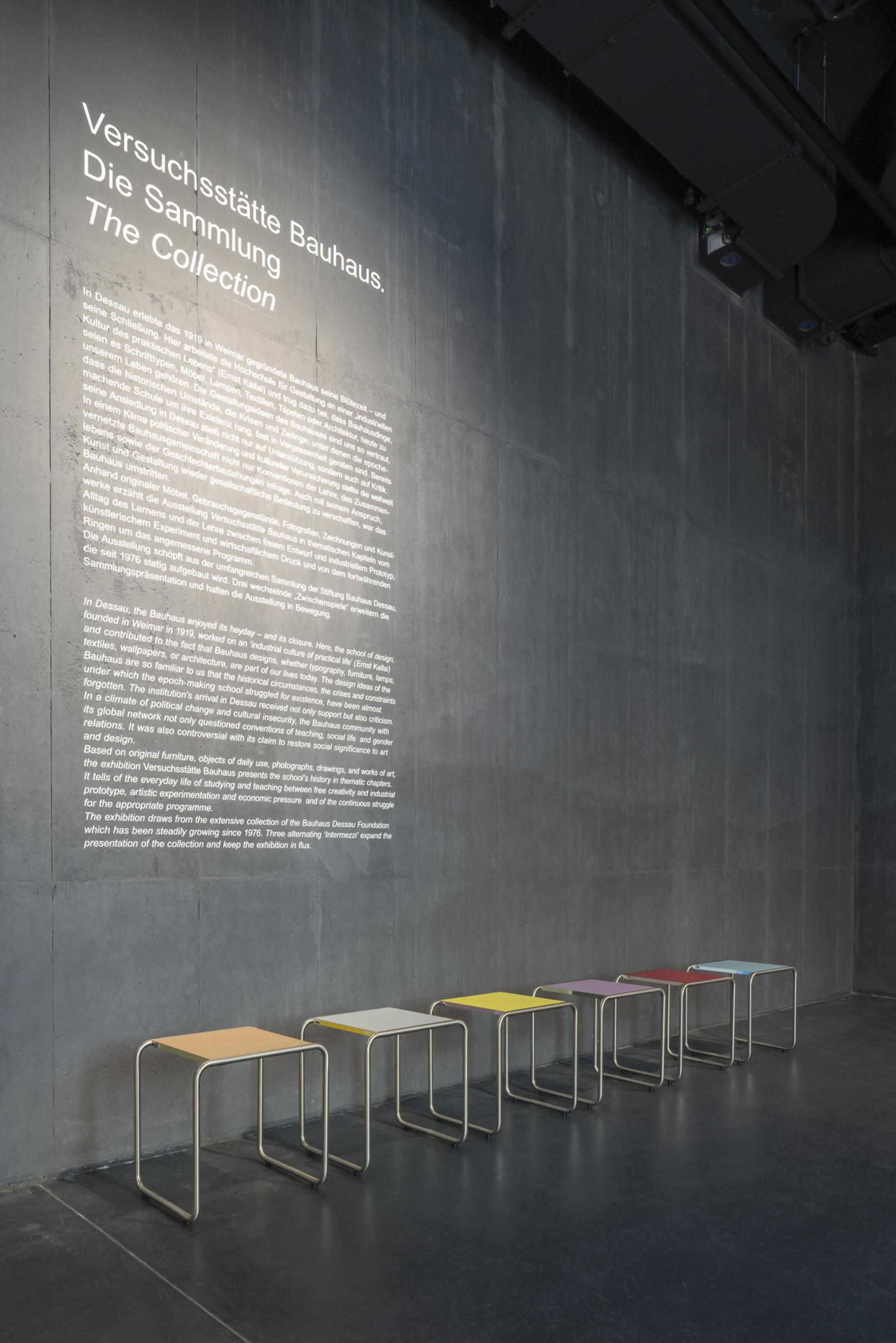 Colorful tubular steel stools by Jay Gard displayed against a concrete wall at the Bauhaus Museum Dessau exhibit.