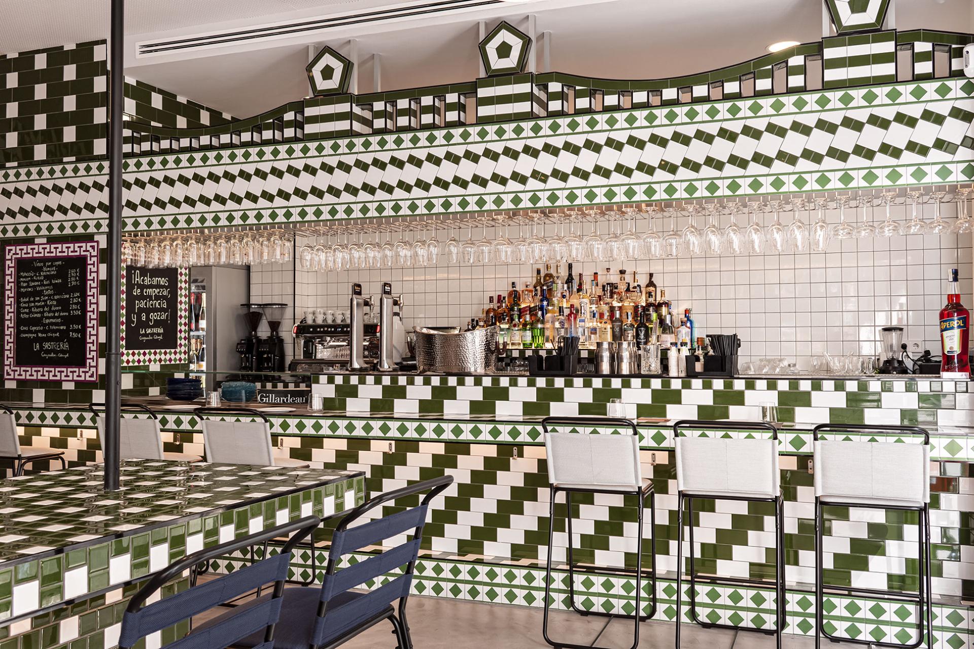 Vibrant green and white tiled bar area in La Sastrería restaurant, showcasing a variety of spirits and a modern design.