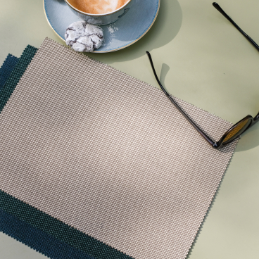 Two-tone woven fabric swatches from Agua's Zephyr collection alongside a cup of coffee and sunglasses on a green table.