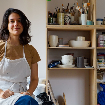 Bucharest ceramicist Sandra Berghianu poses in her studio surrounded by handmade pottery and art supplies.