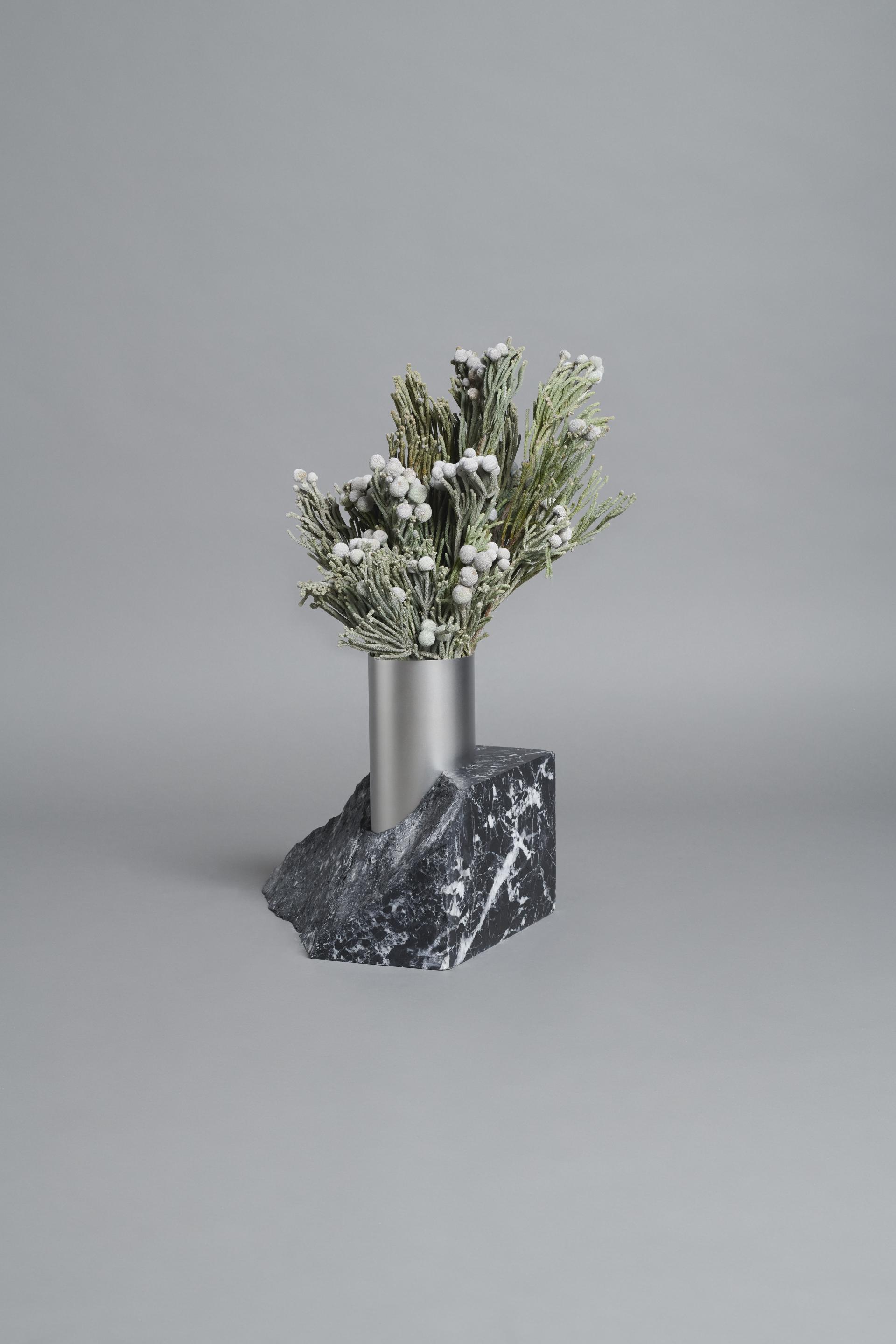 Stylish arrangement of artificial greenery in a sleek metallic vase, resting on a textured black marble base.