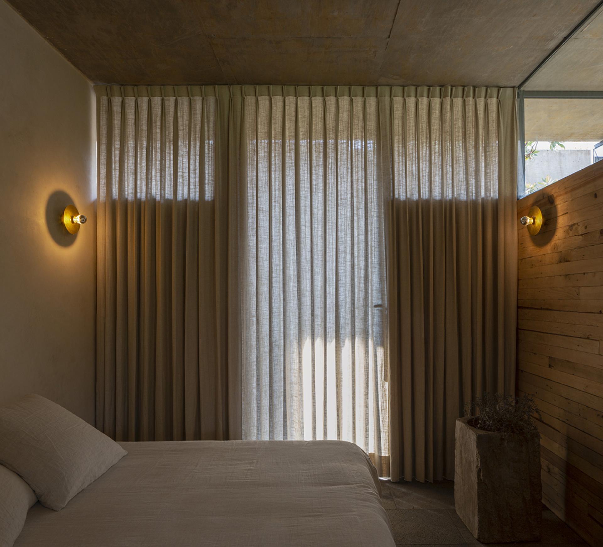 Cozy bedroom in Avocado House featuring sheer curtains, natural wood accents, and warm lighting for a serene atmosphere.