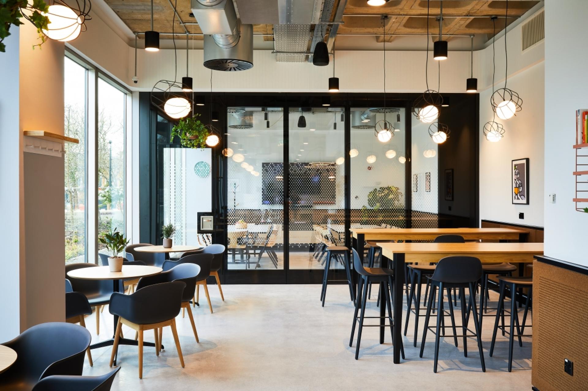 Modern workplace cafe with stylish furniture, natural light, and greenery promoting collaboration and creativity in a contemporary environment.