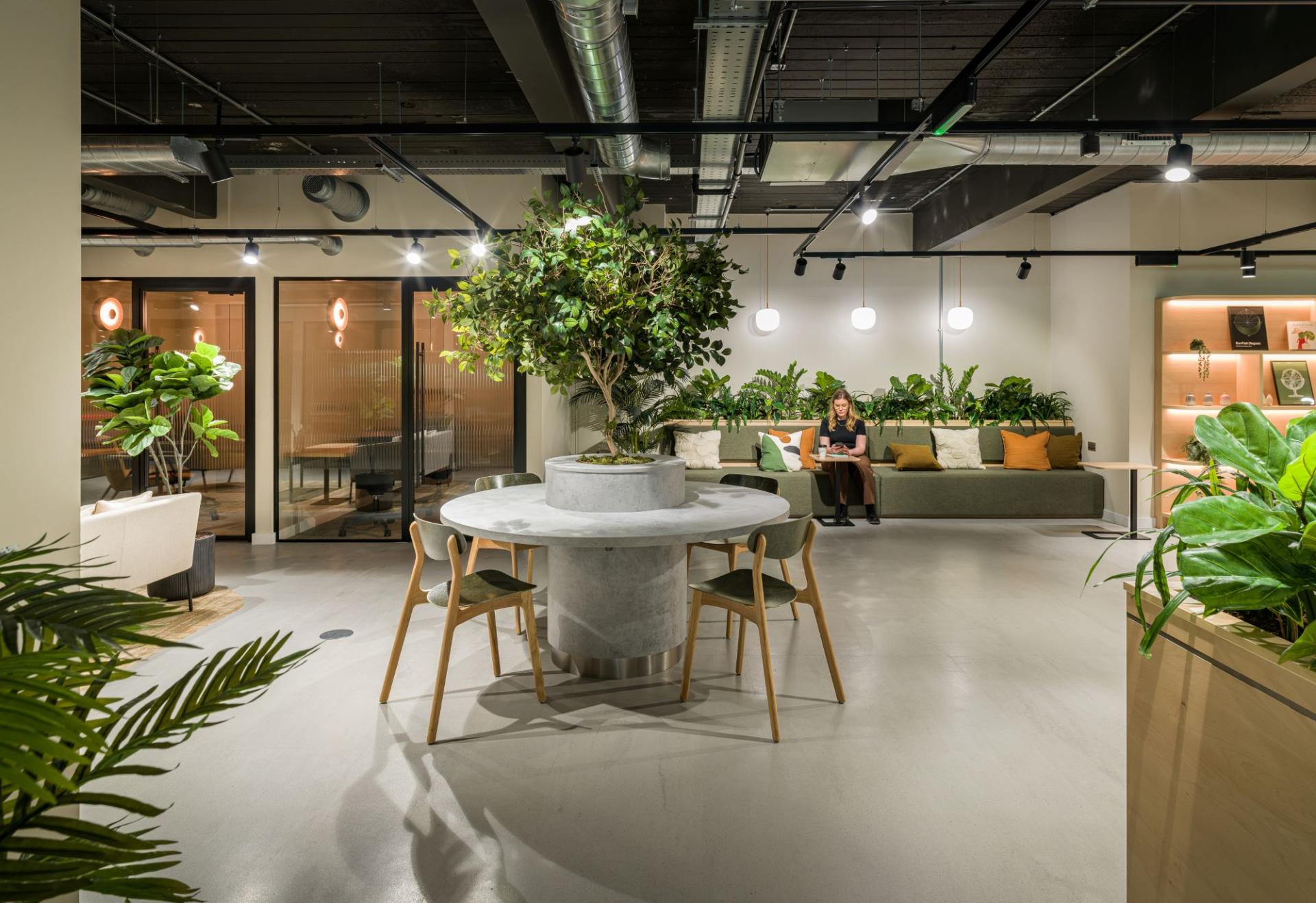 Modern office interior with greenery, a circular table, and a seating area, showcasing SpaceInvader's design at Glasshouse, Alderley Park.