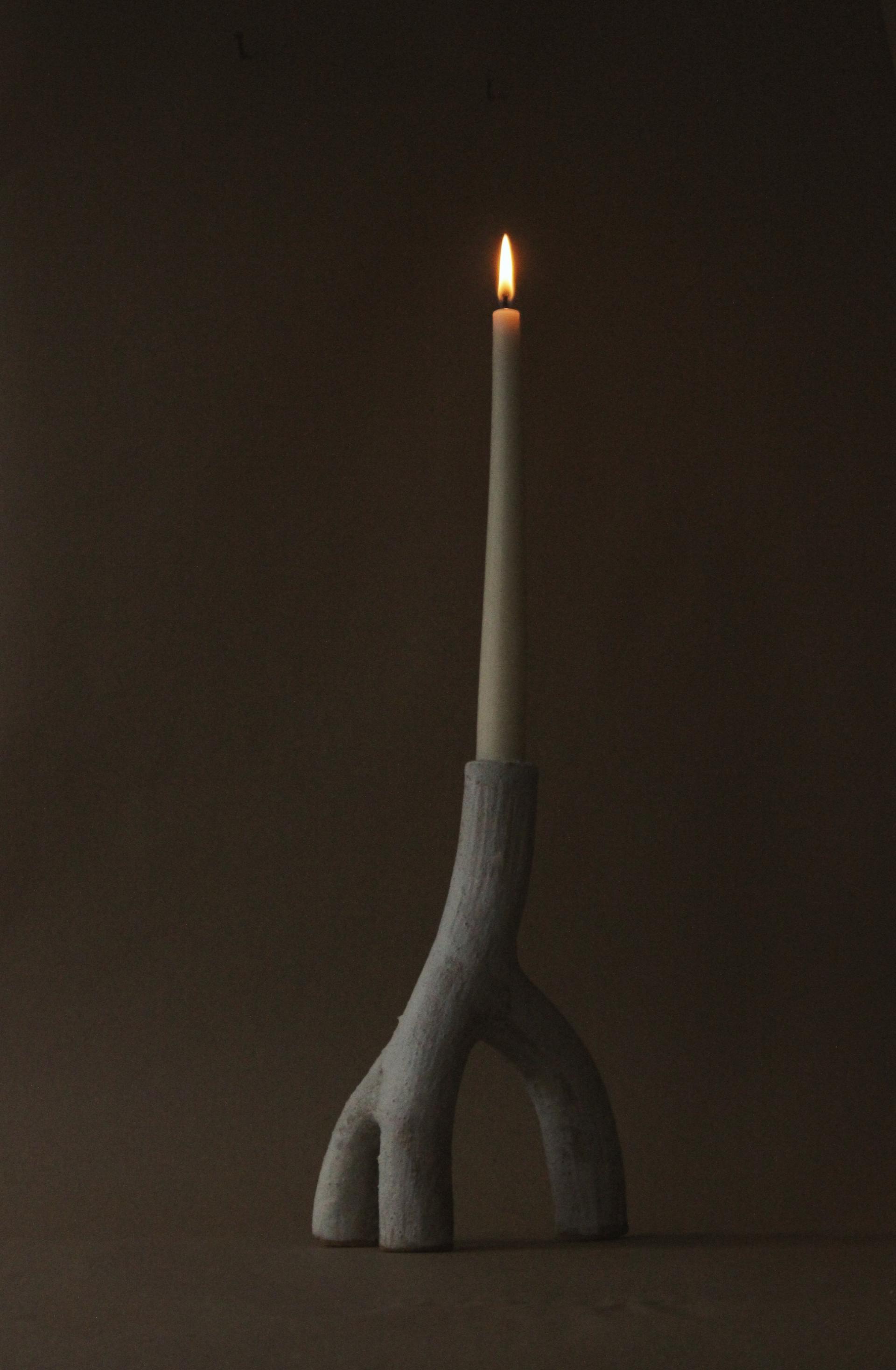 A unique candle holder resembling a branch, holding a lit candle against a neutral background, celebrating Glasgow's creative craftsmanship.