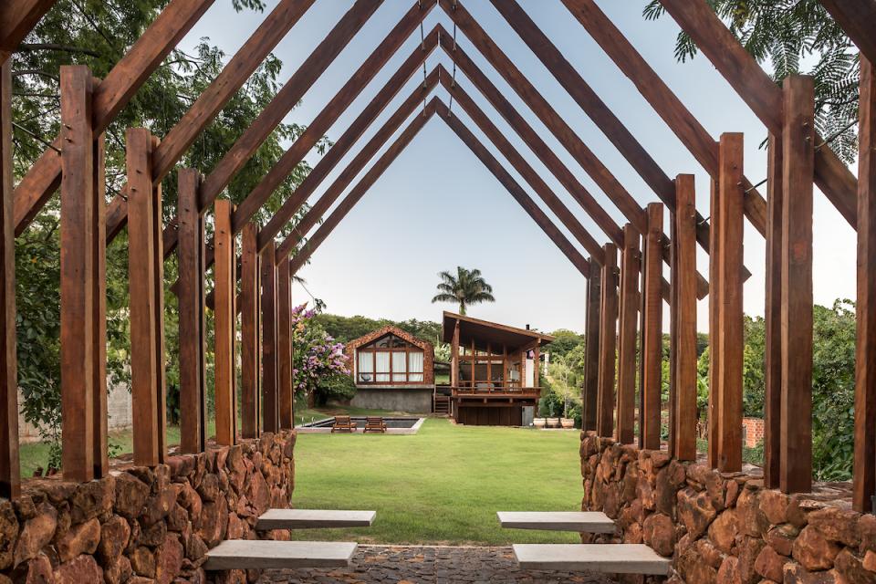 Modern wooden architecture of The Lake House framed by a stone pathway, surrounded by lush greenery in Brazil.