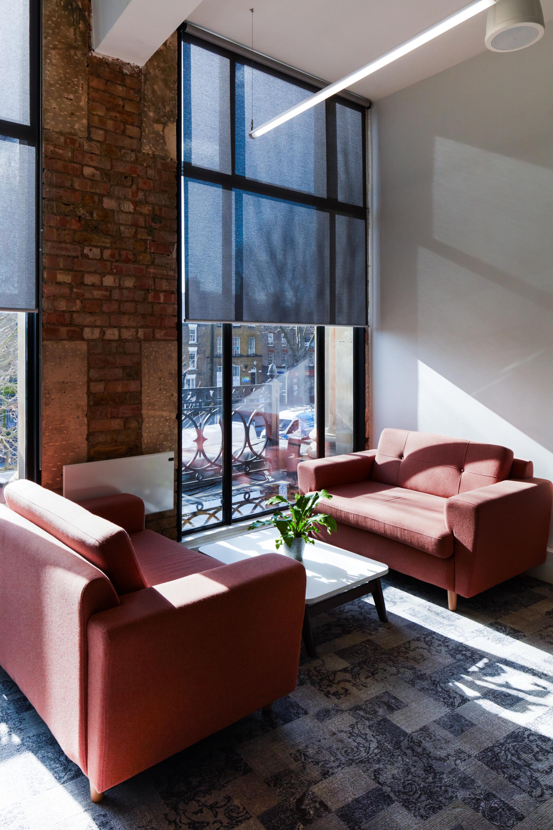 Stylish lounge area with two red sofas and a small table, featuring large windows and natural light at Queen Mary University.