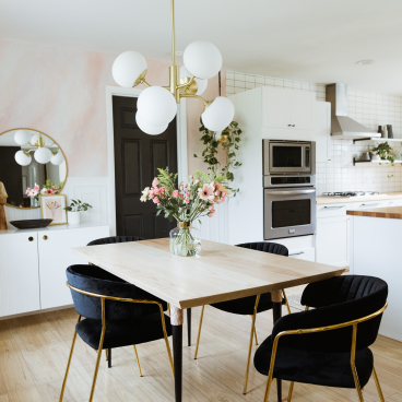 Modern chandelier by Hudson Valley Lighting Group illuminates a stylish dining area with a wooden table and plush black chairs.