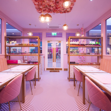Stylish pastel pink nail salon interior featuring marble tables, plush seating, and an array of nail polishes.